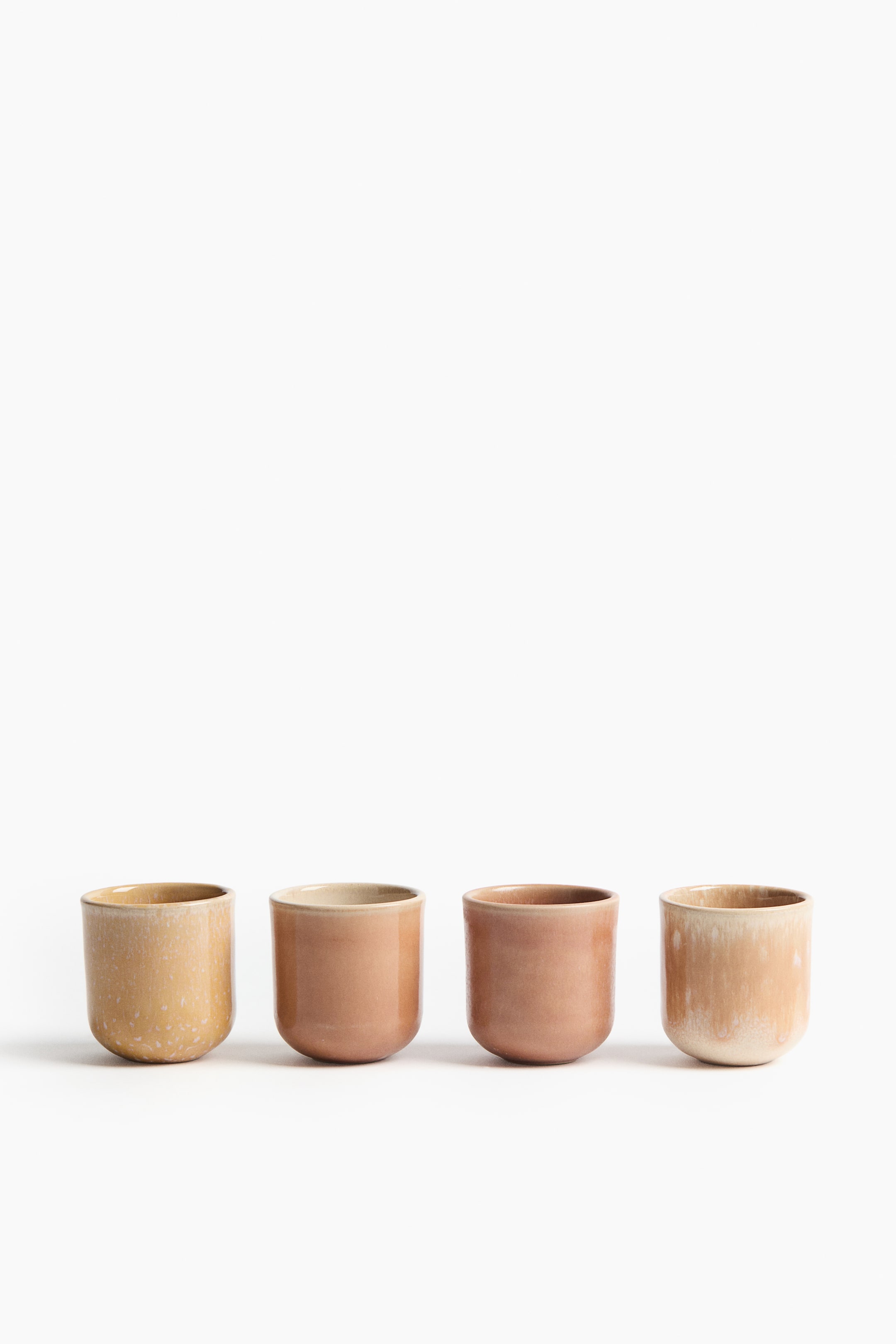 Ver imagen más grande: Un conjunto de cuatro tazas de espresso de gres esmaltado se muestra desde el frente, cada una con una forma clásica y un acabado artesanal. Las tazas exhiben una coloración variada, creada por un esmalte reactivo que le da a cada una una apariencia única.