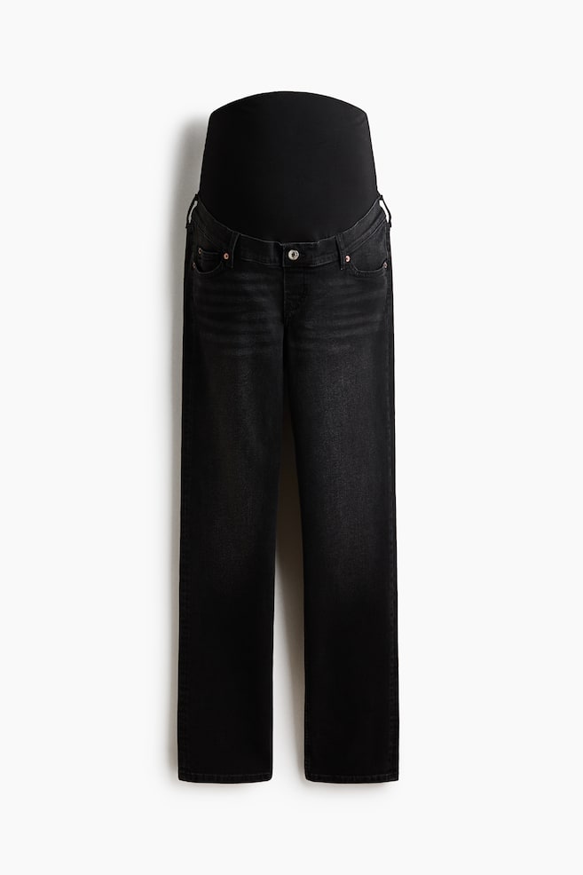 Washed black maternity jeans are facing forward, featuring a wide, high, black elasticized belly panel. They are displaying a button closure, front pockets with rivets, and a straight-leg cut. - 1
