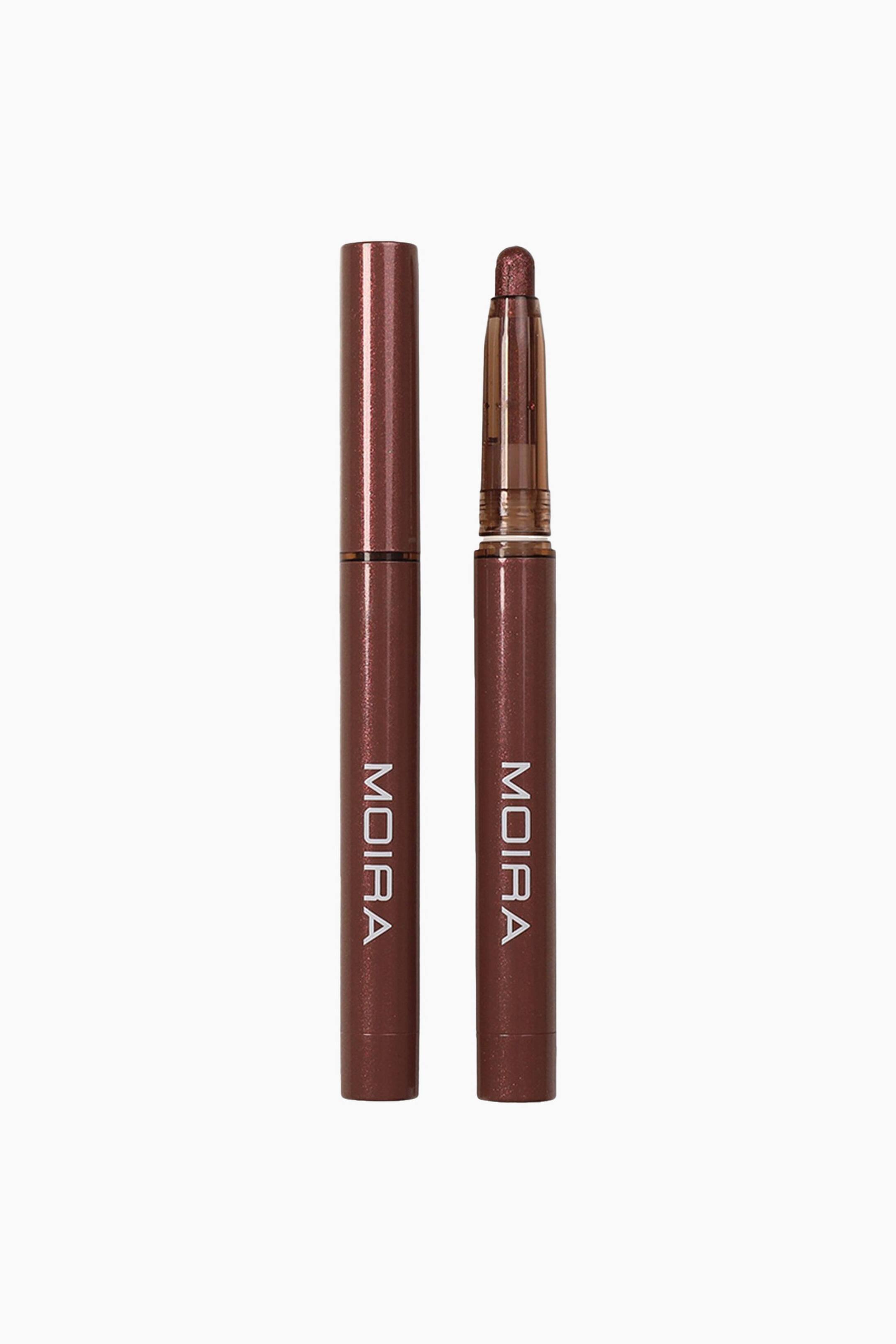 Vis større bilde: Stellar Glaze Stick Shadow står loddrett i to versjoner: en pen med kork til venstre og en pen uten kork til høyre, begge med metalliske bronsebrune hylstre og en hvit, vertikal logo. Pennen uten kork til høyre viser en avrundet, skimrende bronsefarget øyenskyggetupp som stikker ut fra en gjennomsiktig, tonet plastholder.
