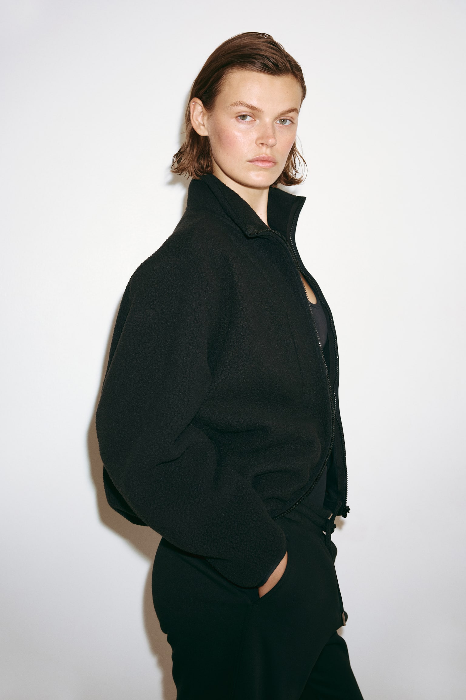 A black fleece jacket is displaying its front, featuring a full-zip closure, a stand-up collar, and long sleeves. It is made of a textured fleece material and includes curved seam details on the front panels. - 1