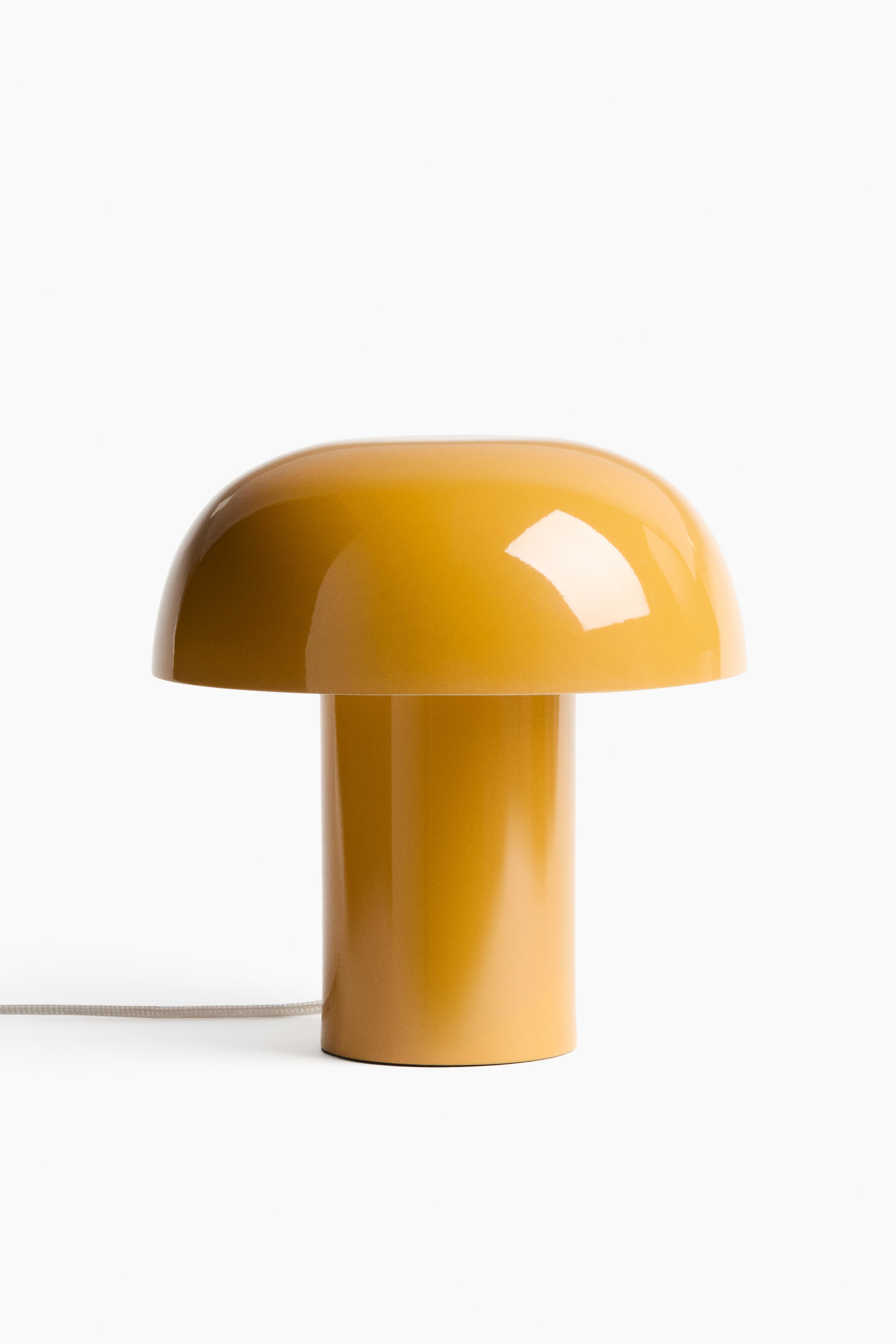 View larger image: A contemporary table lamp faces forward, showcasing a glossy yellow finish and a soft, mushroom-inspired shape, consisting of a cylindrical base and a domed shade. A light-coloured, fabric-covered cord emerges from the base.