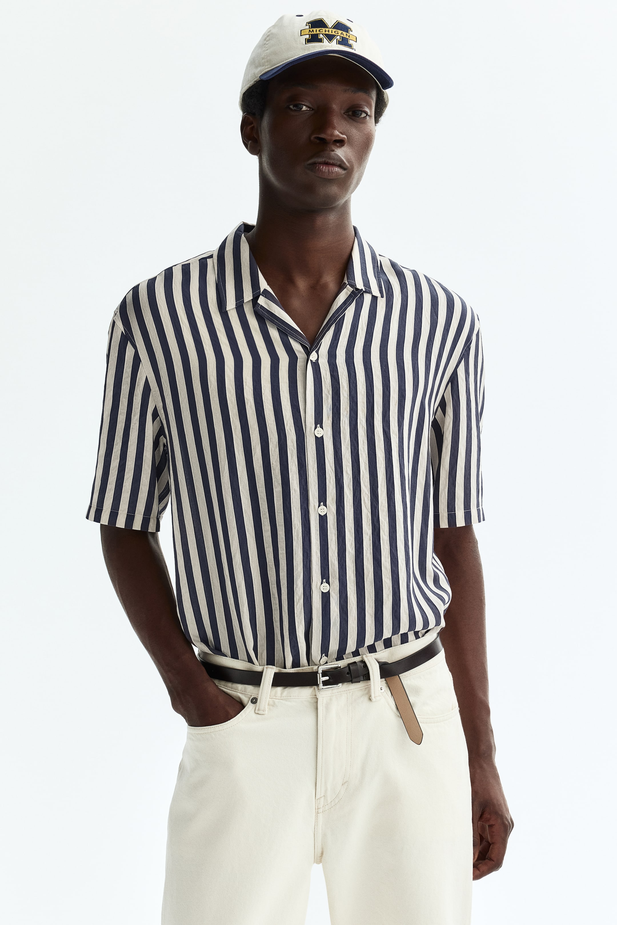 Agrandir l'image: Une chemise à manches courtes avec des rayures verticales bleu marine et blanc cassé sur un tissu froissé. Elle est conçue avec un col cubain et une fermeture à boutons sur le devant avec des boutons blancs.