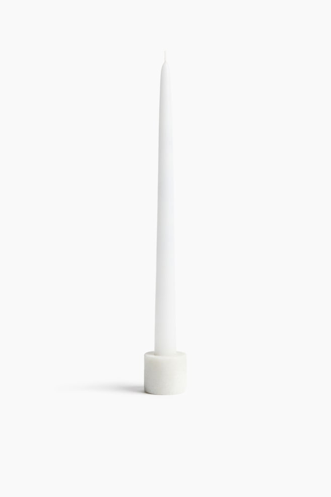 A tall, white tapered candle stands upright, narrowing to a fine point with a visible wick at the top. The candle is set inside a small, cylindrical white marble holder with subtle grey veining. - 1