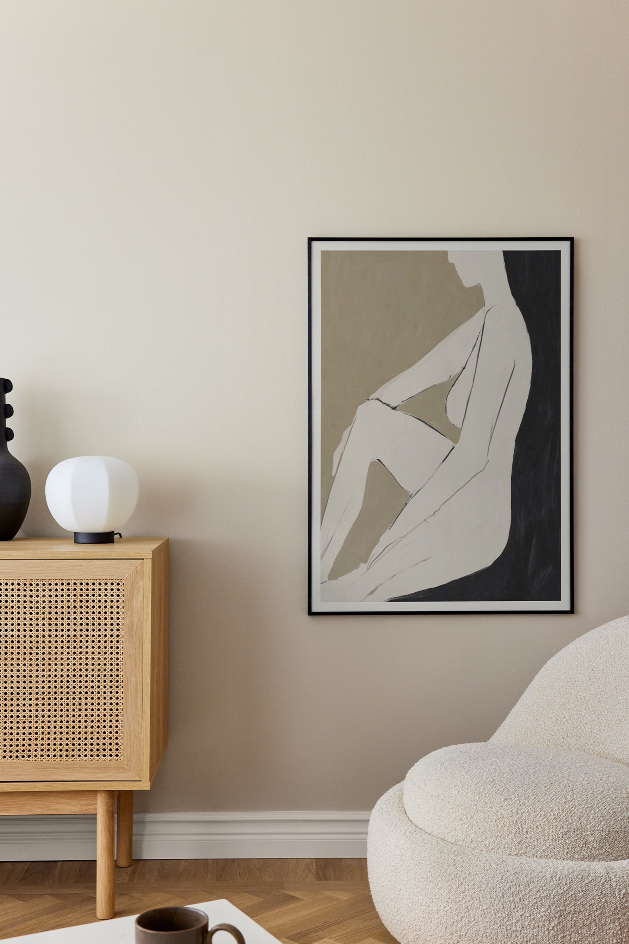 Se større billede: Et indrammet kunsttryk viser en minimalistisk, stiliseret illustration af en siddende nøgen figur i profil, vendt mod venstre. Figuren er gengivet i en lys cremefarve, i kontrast til en delt baggrund med afdæmpet olivengrøn taupe til venstre og mørke kulgrå toner til højre, alt indrammet af en slank sort ramme.