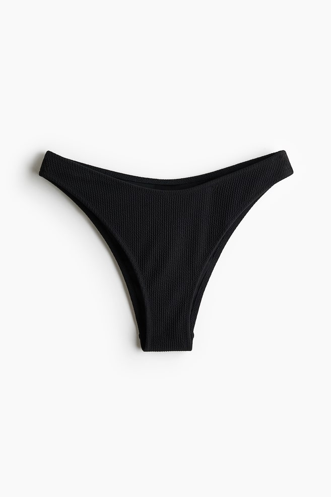 A black textured bikini bottom featuring a low, curved waist and high-cut leg openings at the front. - 1