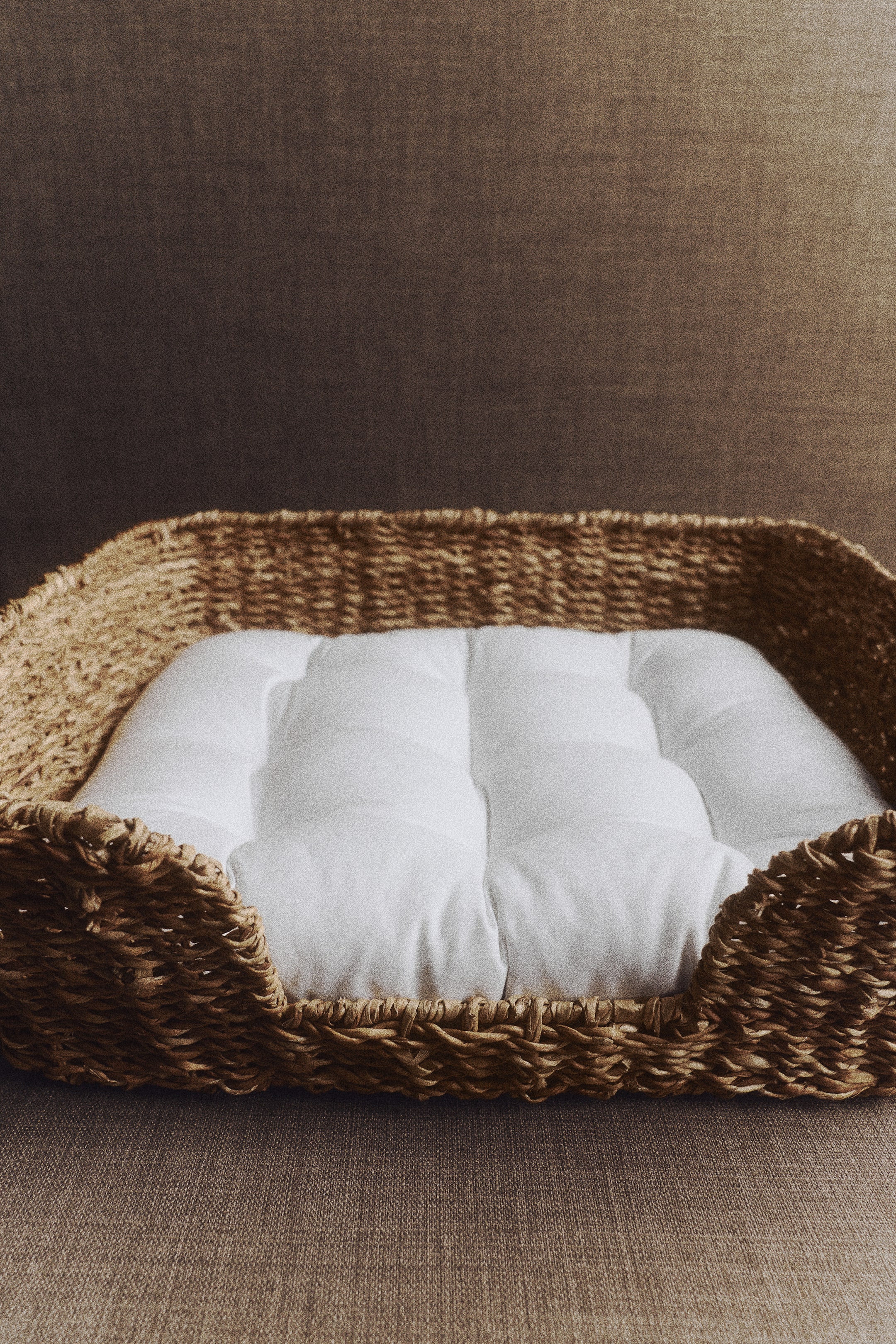 Agrandir l'image: Un panier pour animal tissé est orienté de face, mettant en valeur une structure rectangulaire en fibres naturelles tissées avec une entrée frontale abaissée. Le panier contient un coussin moelleux blanc capitonné, parfaitement ajusté à l’intérieur.