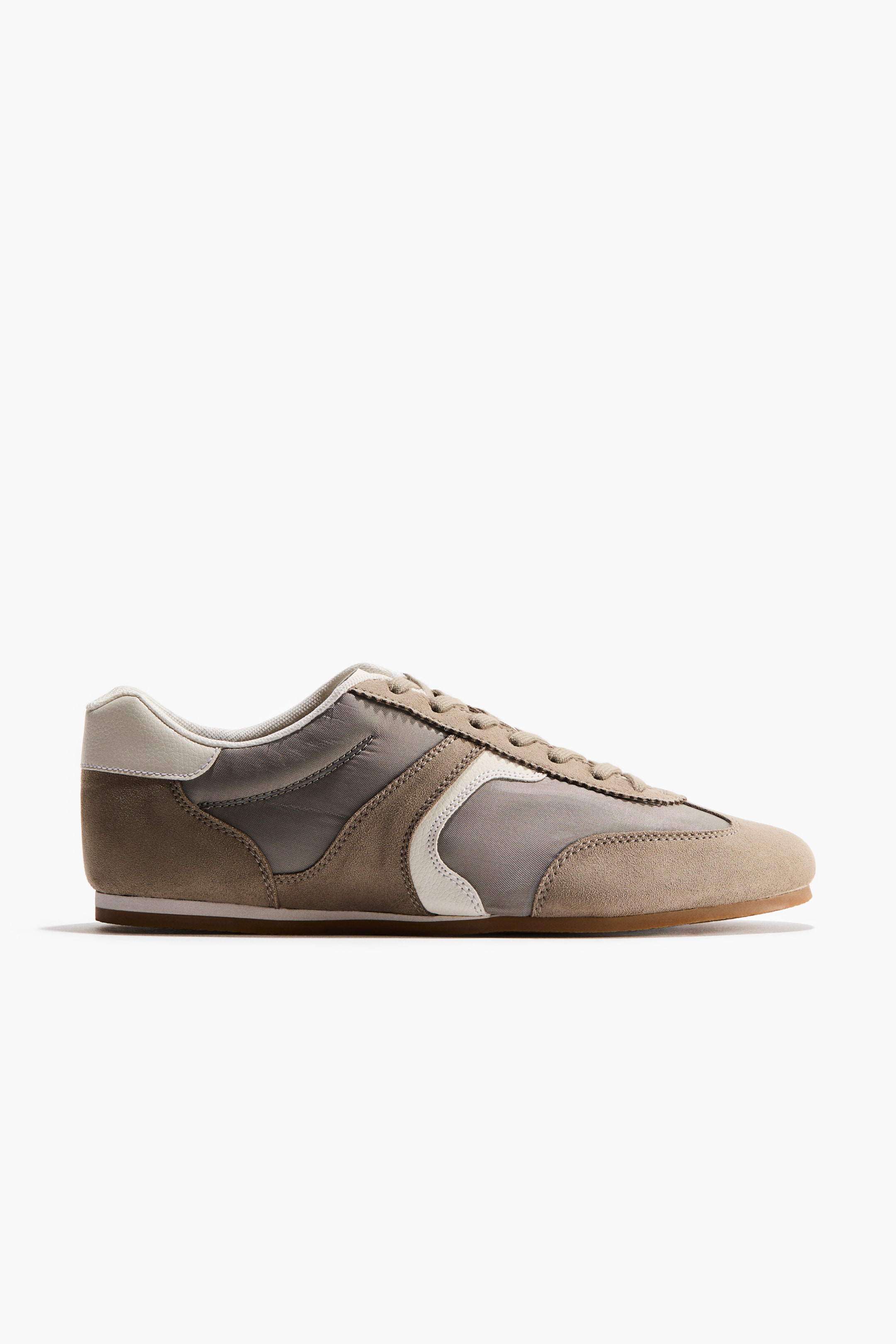 View larger image: A trainer is facing right in a side view, featuring tan suede and grey fabric panels, a padded top edge, and a tongue with lacing at the front. A white curved detail is appearing on its side.