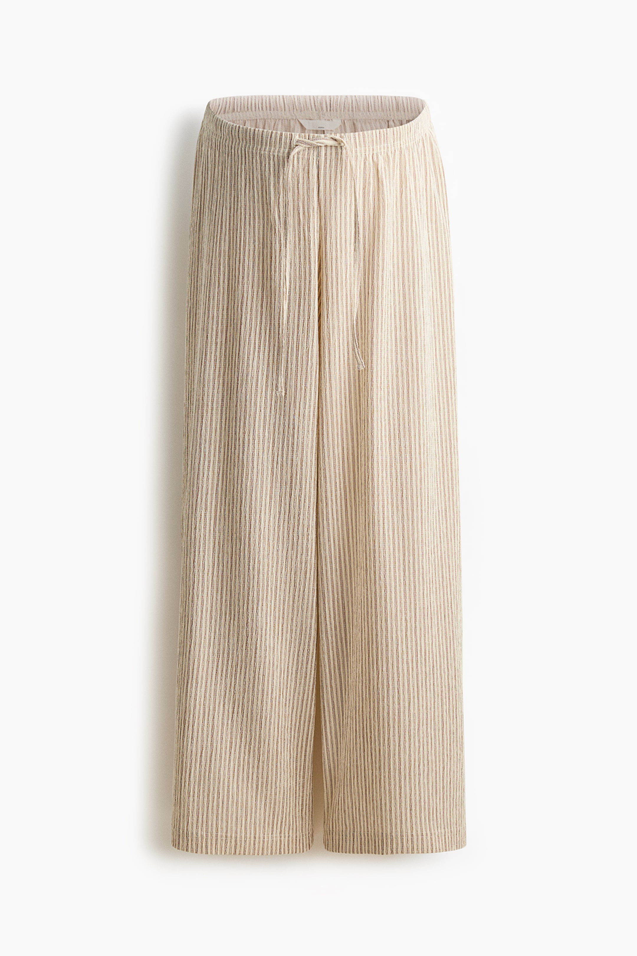 Größeres Bild anzeigen: Die Hose wird in einer Vorderansicht präsentiert und zeigt eine hellbeige Farbe mit feiner vertikaler Rillenstruktur. Sie verfügt über eine weite Beinsilhouette und einen elastischen Bund mit einem natürlichen Kordelzug in der vorderen Mitte.