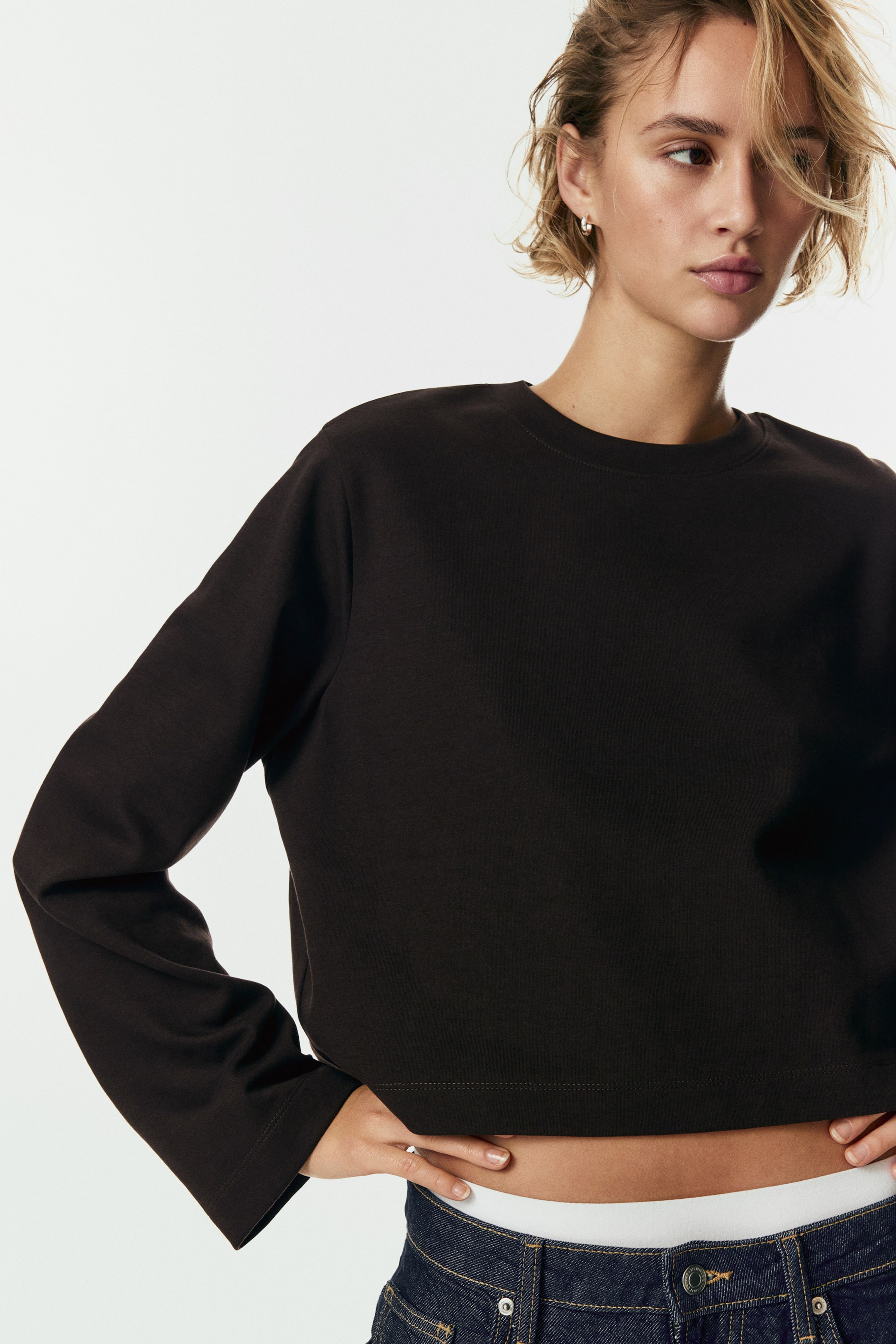 View larger image: A dark brown long-sleeved top is featuring a crew neck and a relaxed fit. The top is designed with long, loose sleeves and simple cuffs, and is cut in a cropped style, ending above the waist.