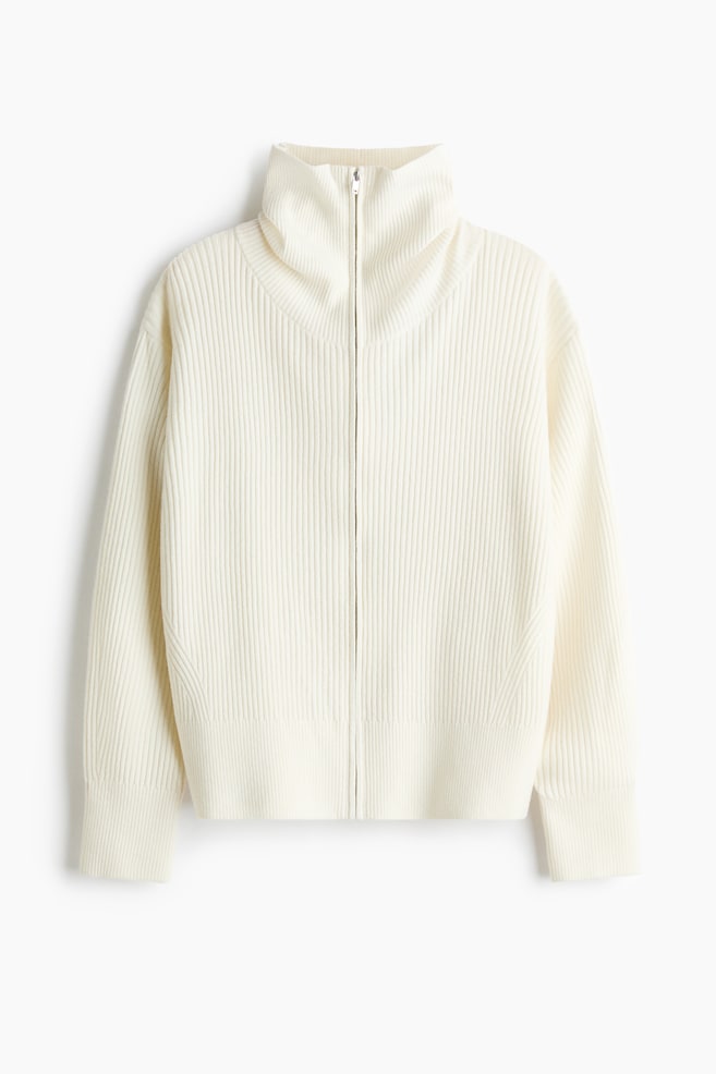 An off-white ribbed cardigan is facing the front, featuring a high funnel neck and a full-length front zip closure. The cardigan is showcasing a vertical ribbed-knit pattern with wide ribbed cuffs and a matching ribbed hem. - 1