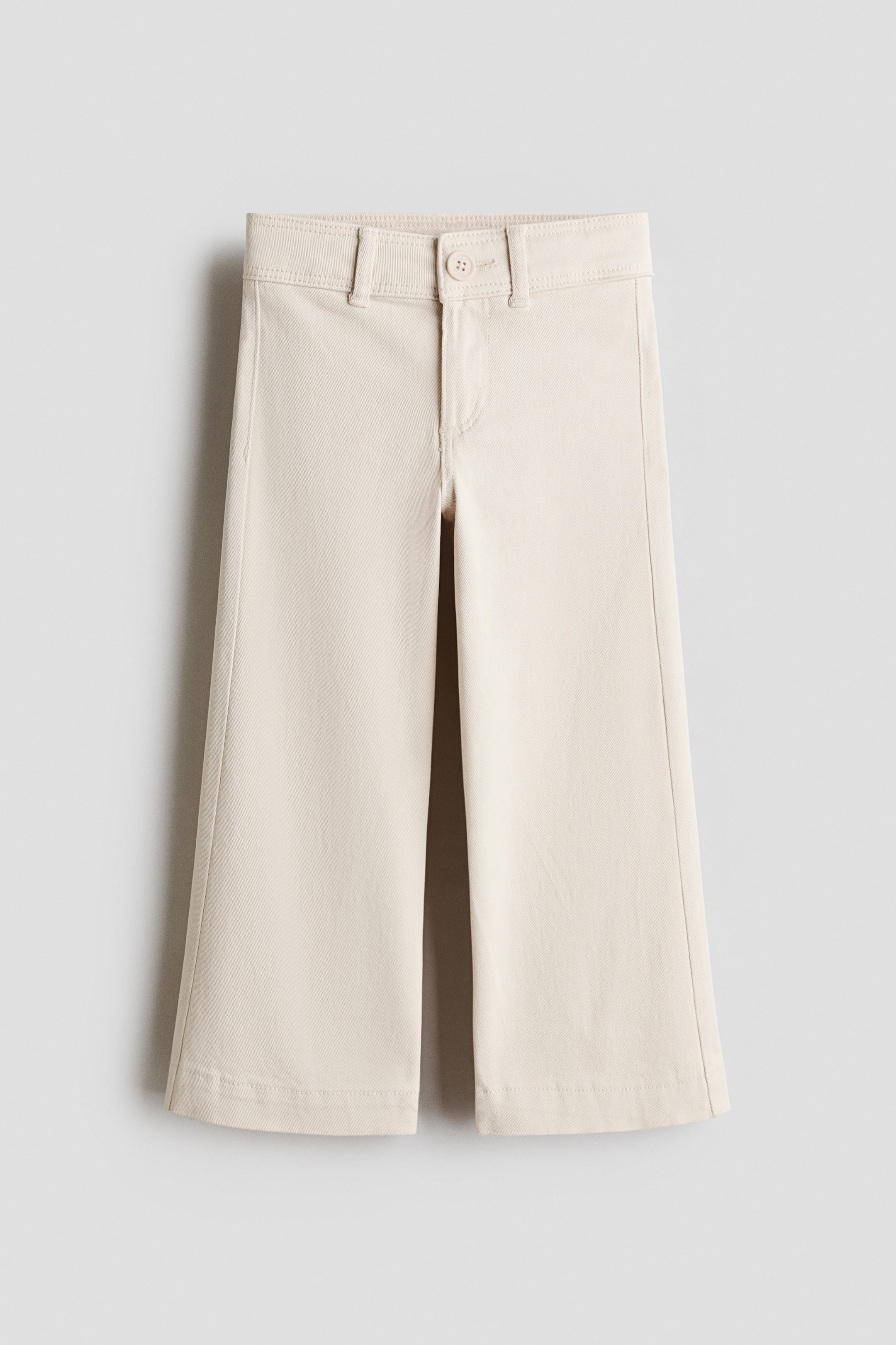 View larger image: Light beige trousers are facing front, displaying a wide, flared leg design. The waistline features belt loops, a button closure, and a zip fly.