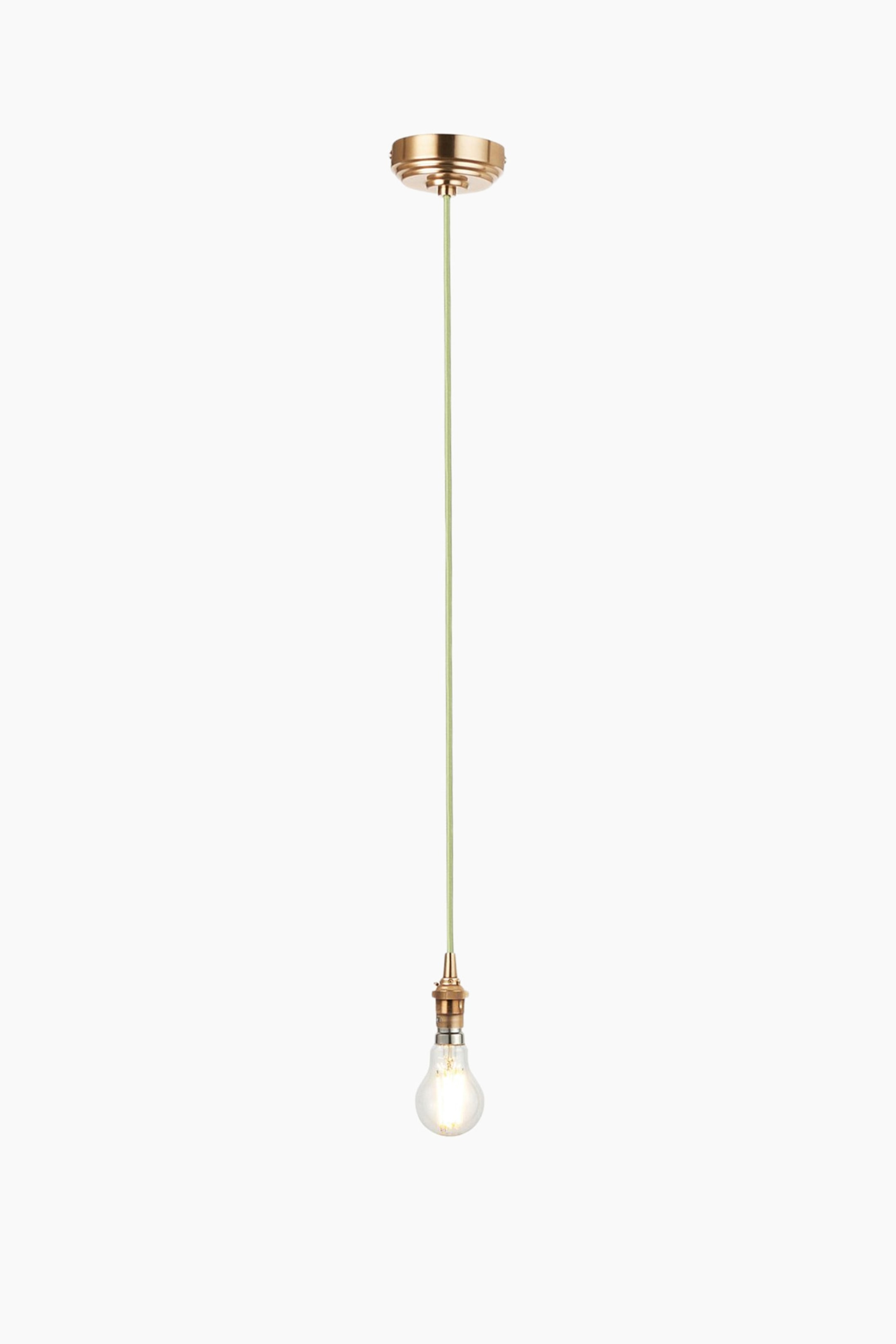 View larger image: A pendant light is hanging vertically, featuring a round, tiered brass ceiling canopy, a light green fabric-covered cord extending downwards, and a brass-toned bulb holder with a clear, glowing bulb facing downwards.