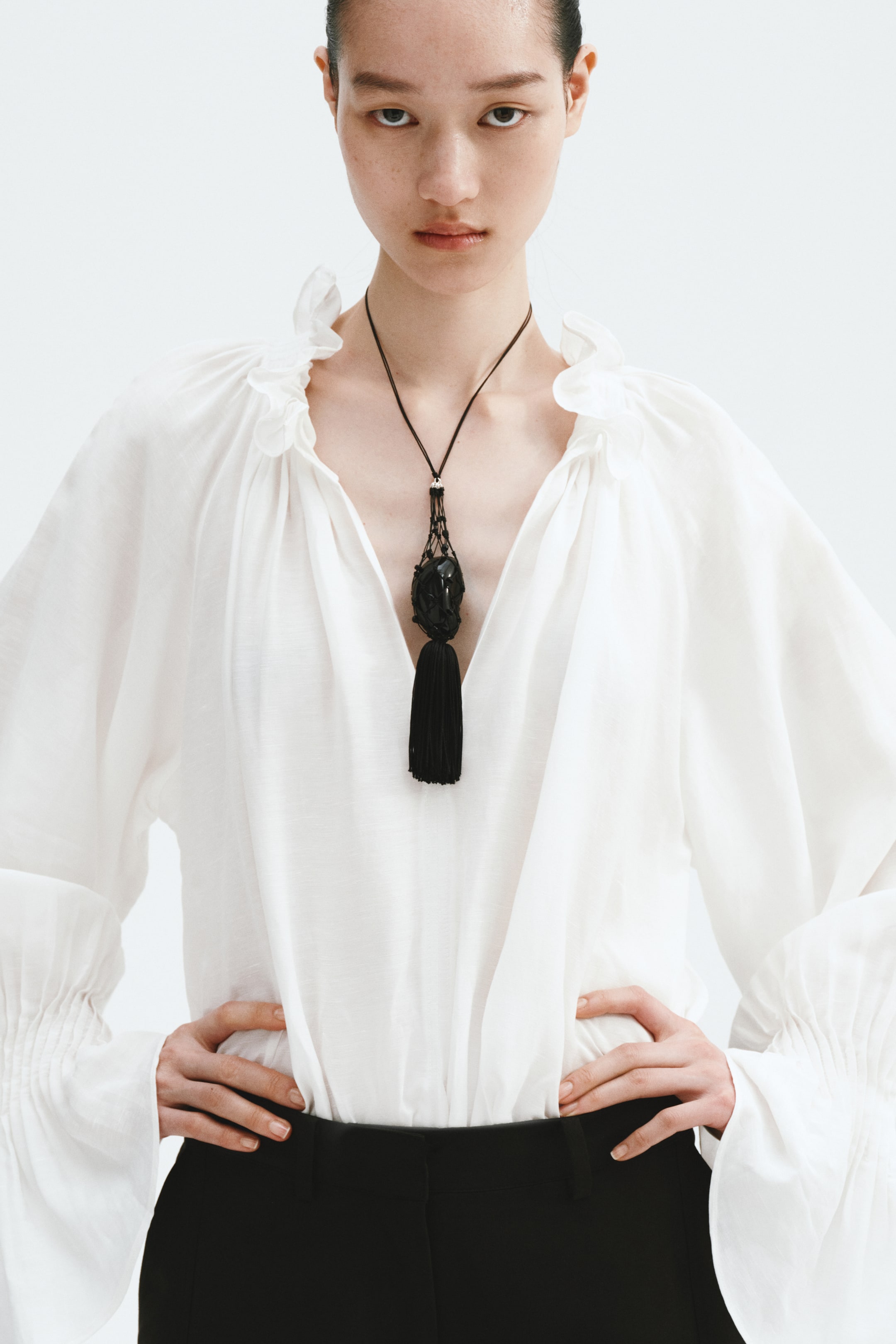 View larger image: The white blouse features a relaxed fit with a ruffled V-neckline and long, voluminous sleeves gathered into shirred cuffs.