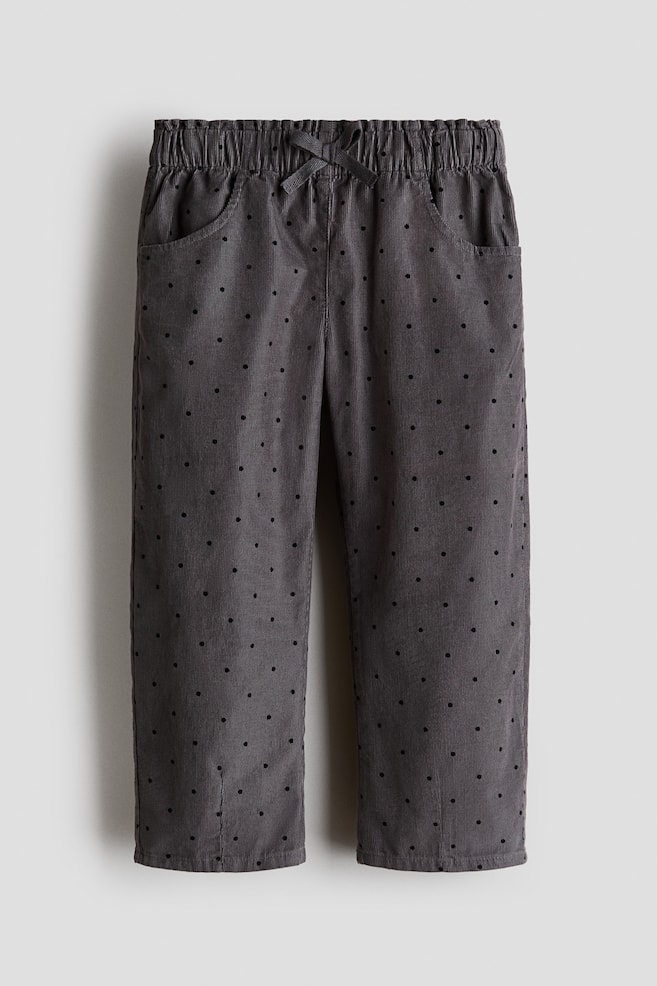 A pair of dark grey corduroy pants is facing front, displaying an all-over pattern of small black polka dots. The pants are featuring a gathered elastic waistband with a decorative matching bow at the center and two curved side pockets. - 1