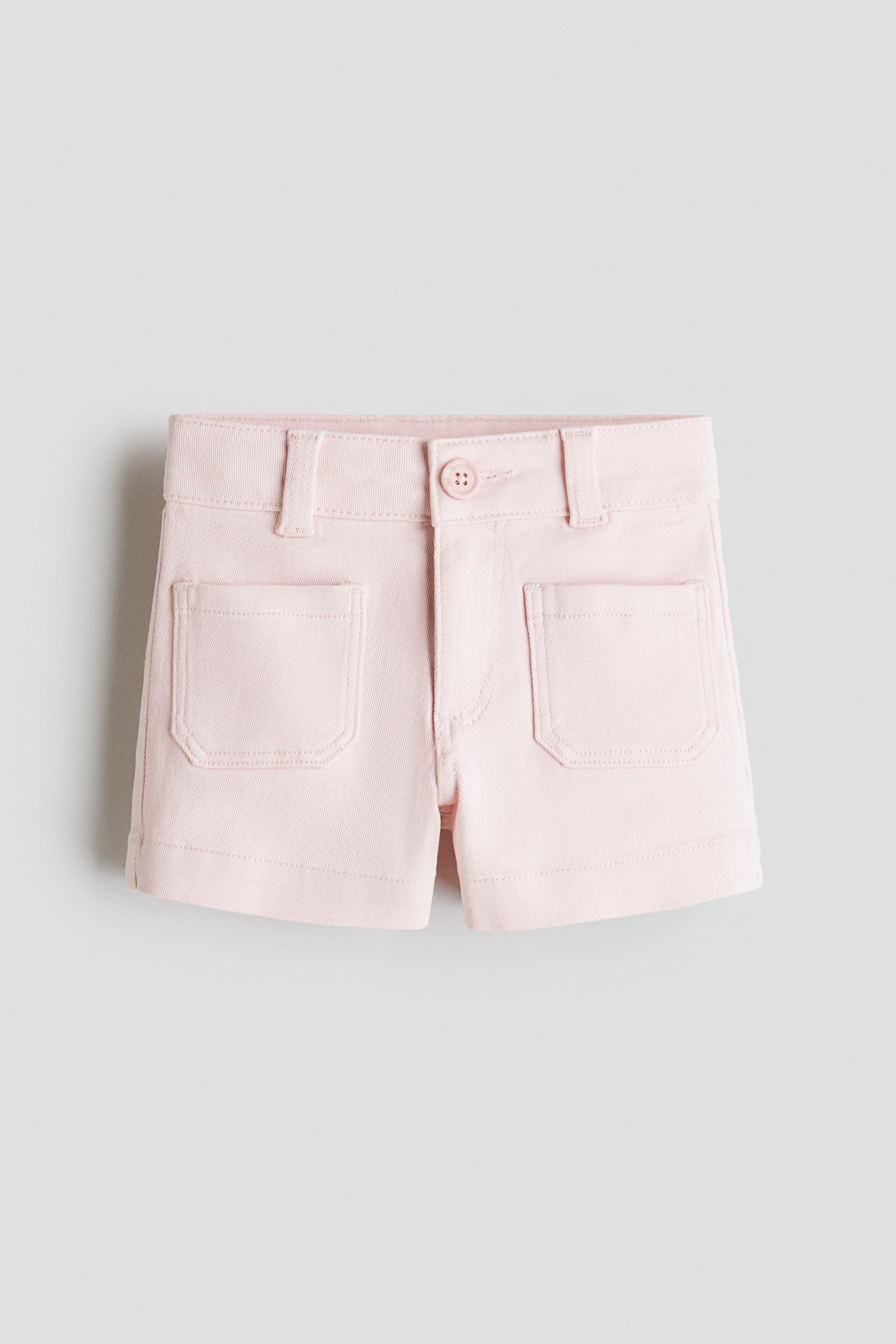 View larger image: Light pink shorts are shown from the front, featuring a waistband with belt loops and a single button fastening. Two rectangular patch pockets are visible on the front, and the leg openings are hemmed.