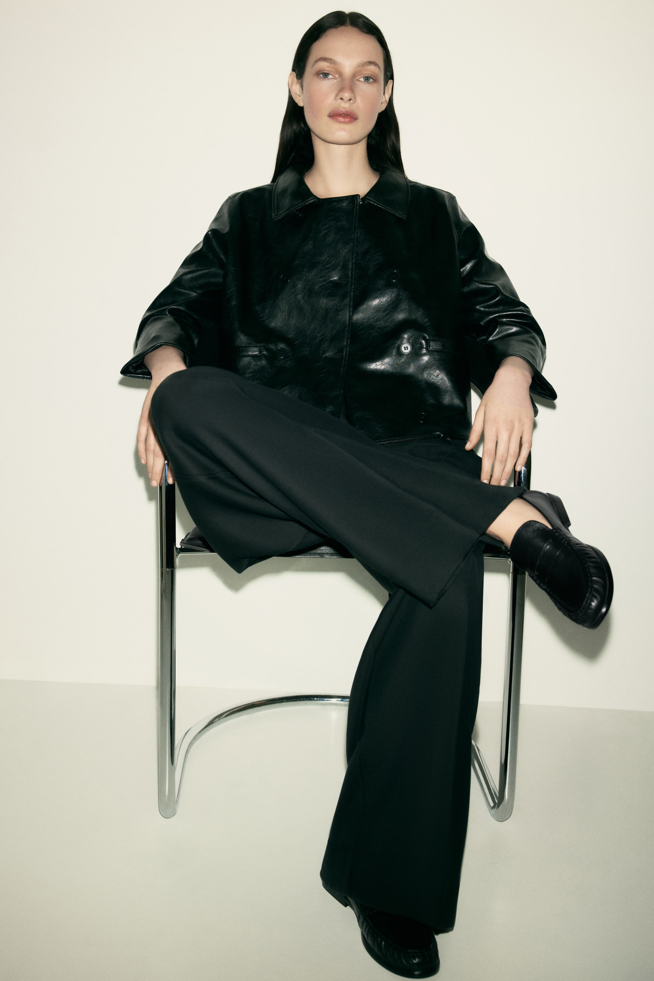 View larger image: The model is wearing black loafers made of soft leather, featuring a moccasin seam at the front. She is sitting with one foot crossed over the other, highlighting one loafer.