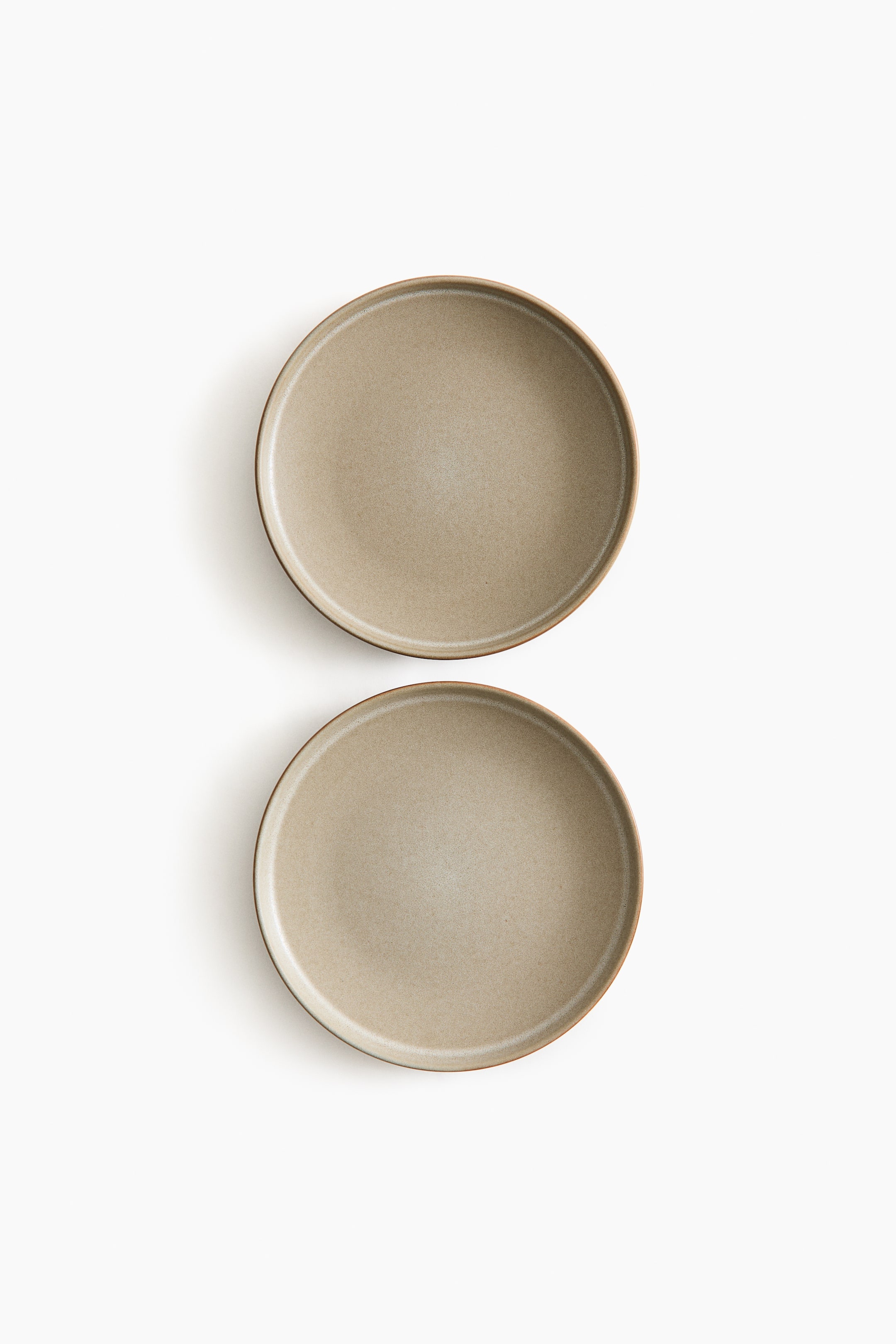 View larger image: Two round stoneware starter plates are showing their front surfaces. They feature a reactive glaze in a light brown hue, creating variegated coloring and giving each plate a unique appearance.
