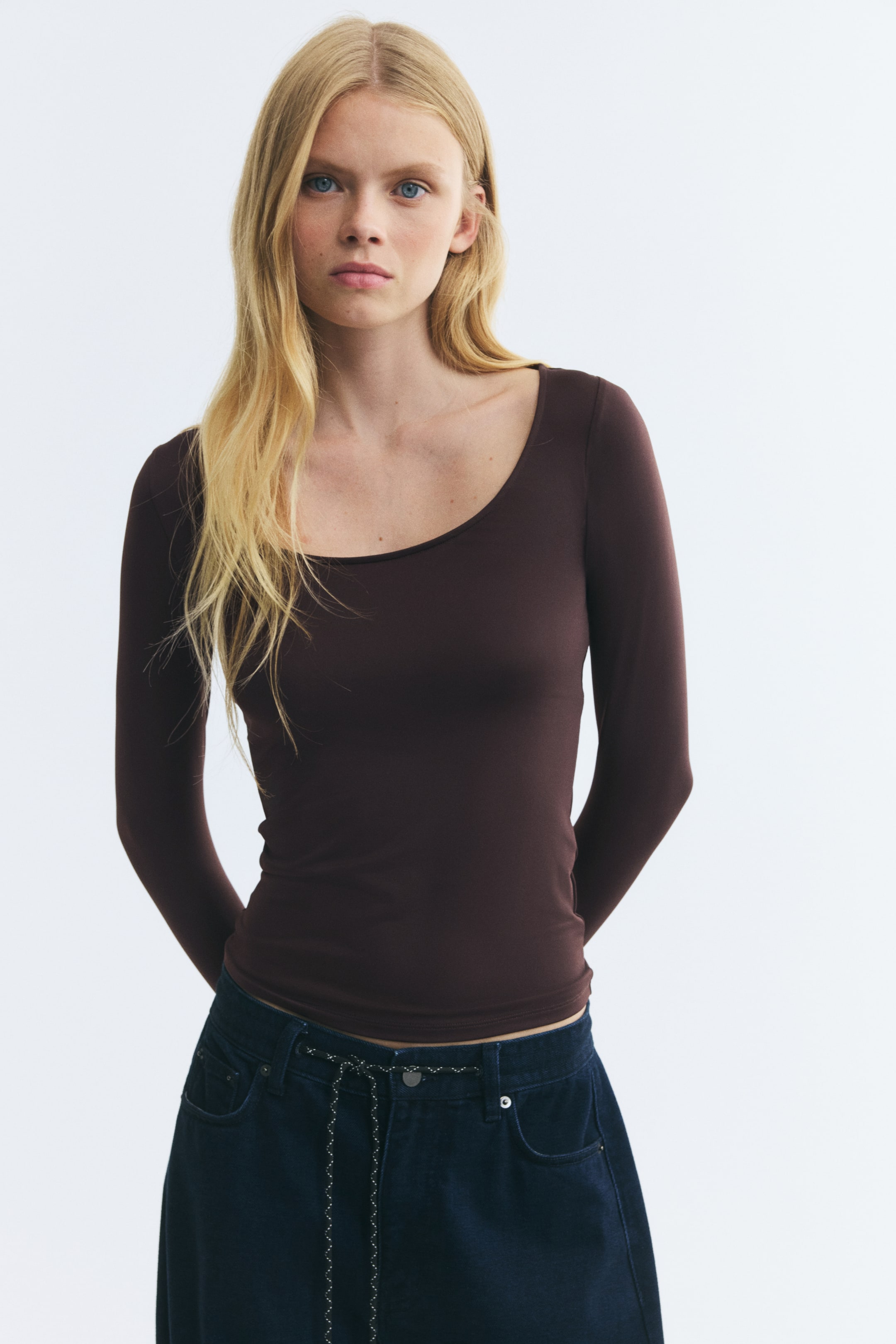 View larger image: A dark brown, fitted microfiber top featuring a scoop neckline and long sleeves is being worn by the model. The top is styled with dark blue denim jeans.