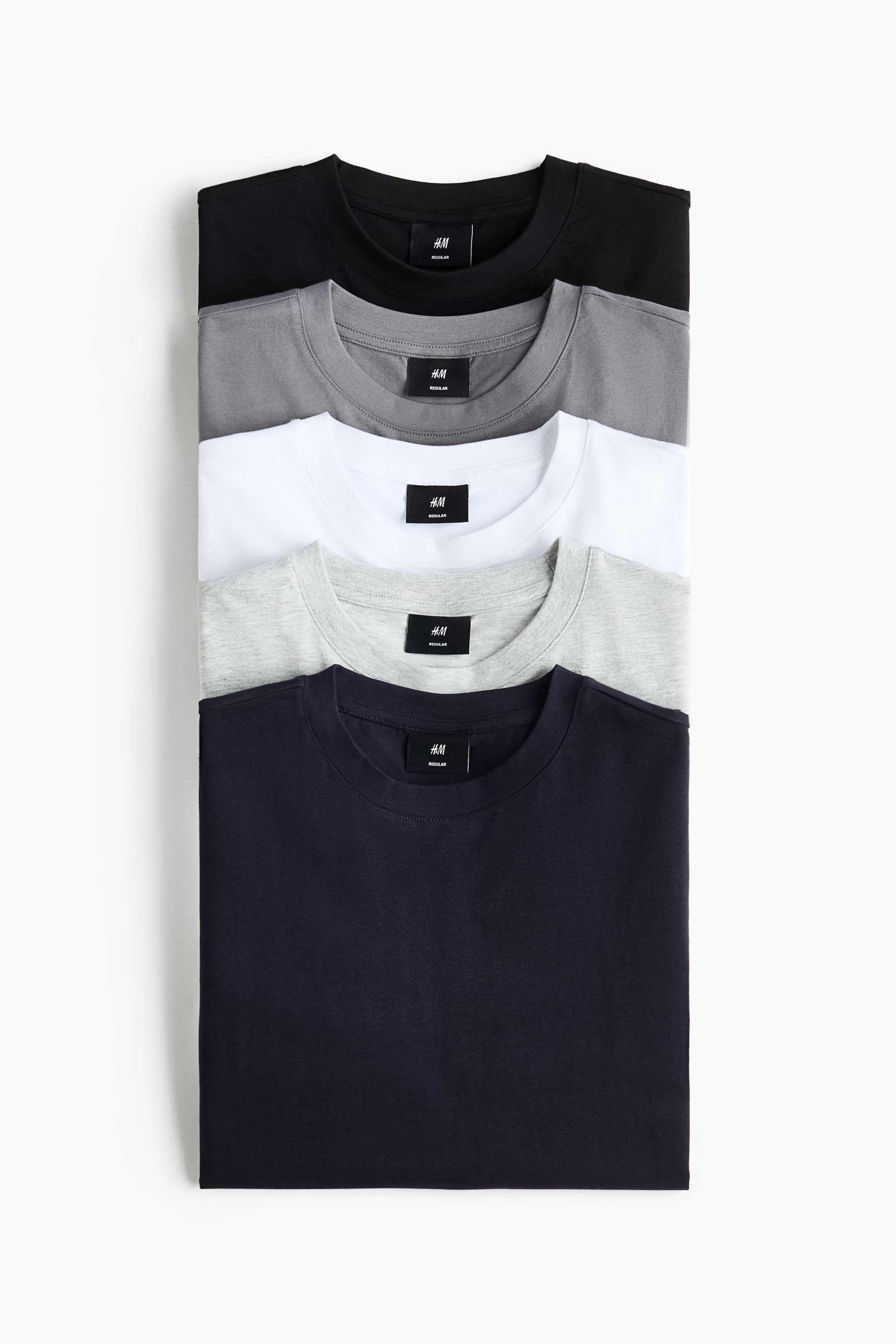 View larger image: Five folded t-shirts are showcased, arranged from top to bottom in black, dark grey, white, light grey, and navy. Each t-shirt features a crew neck with a visible brand tag.