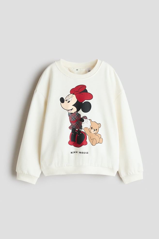 An off-white, oversized sweatshirt is shown from the front, featuring a graphic print of Minnie Mouse holding a teddy bear with the text "MINNIE MOUSE" printed below. The sweatshirt is designed with a ribbed crew neckline, dropped shoulders, long sleeves, and a ribbed hem and cuffs. - 1