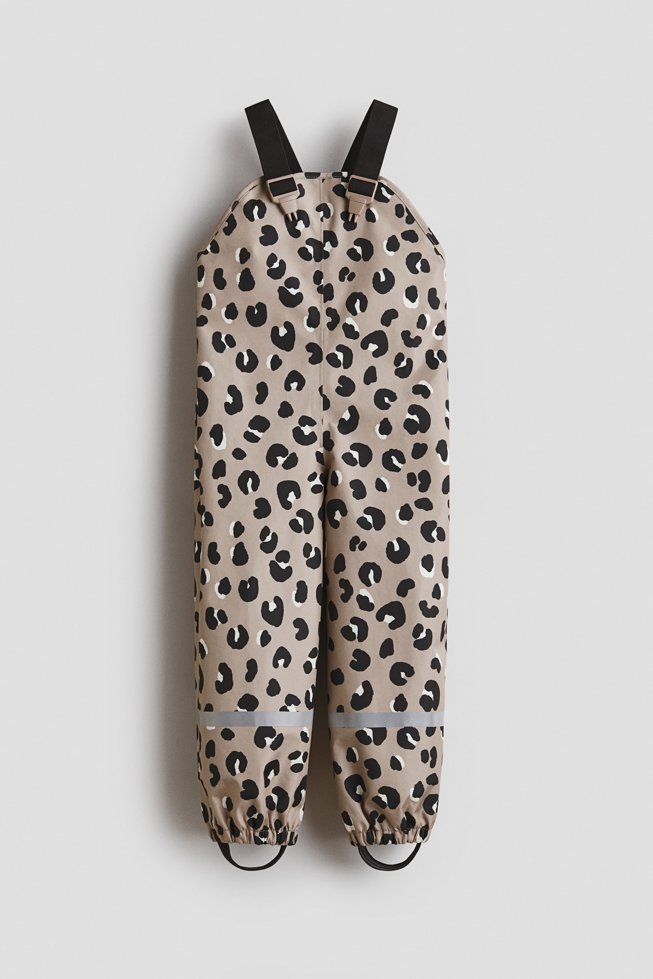 View larger image: Rain overalls showcase a beige backdrop adorned with black and white leopard print spots, presented from the front. They feature black adjustable elastic braces with plastic buckles, reflective strips above the elasticated leg hems, and black detachable elastic foot straps.