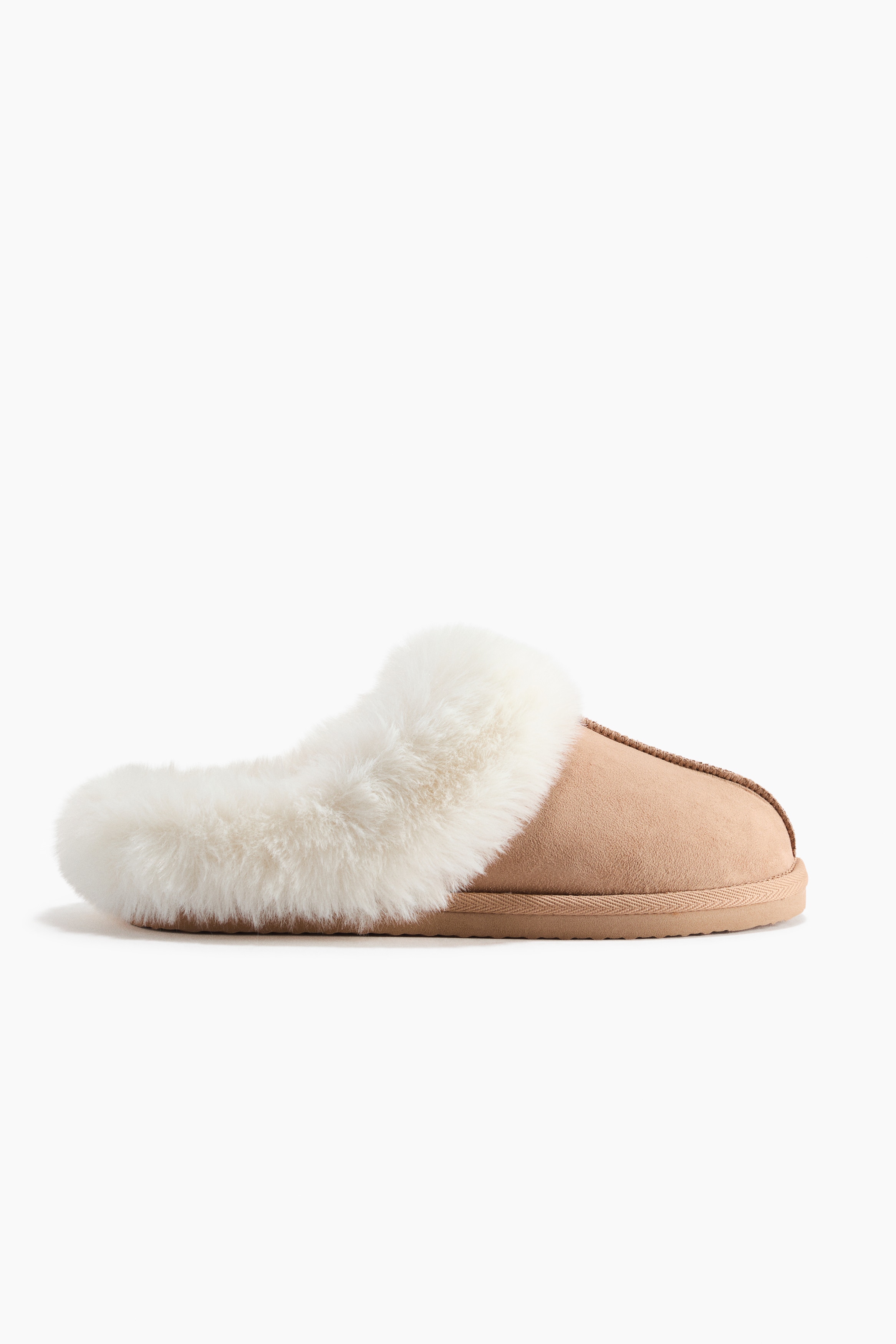 De model draagt slippers met een zachte, geruwde afwerking in lichtbruin, met een centrale naad en een zachte voering van crÃ¨mekleurige stof. Een crÃ¨mekleurige geribde gebreide boord valt over de bovenkant van de slipper.