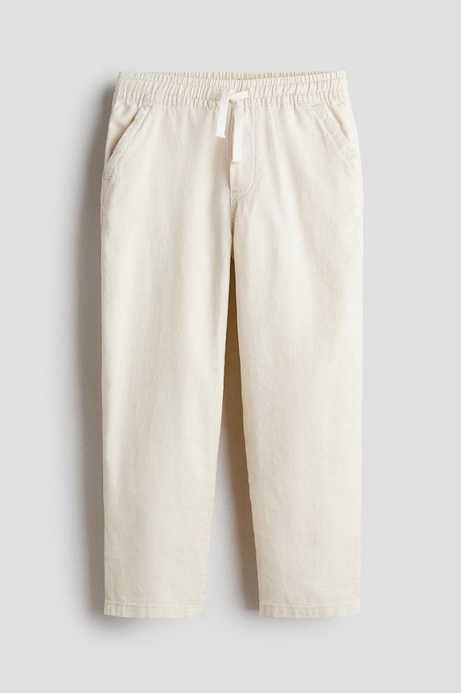 Loose-fit joggers in a textured cotton weave are shown in a front view, featuring an elasticated, drawstring waist with a white drawstring, a faux fly, and diagonal side pockets. - 1