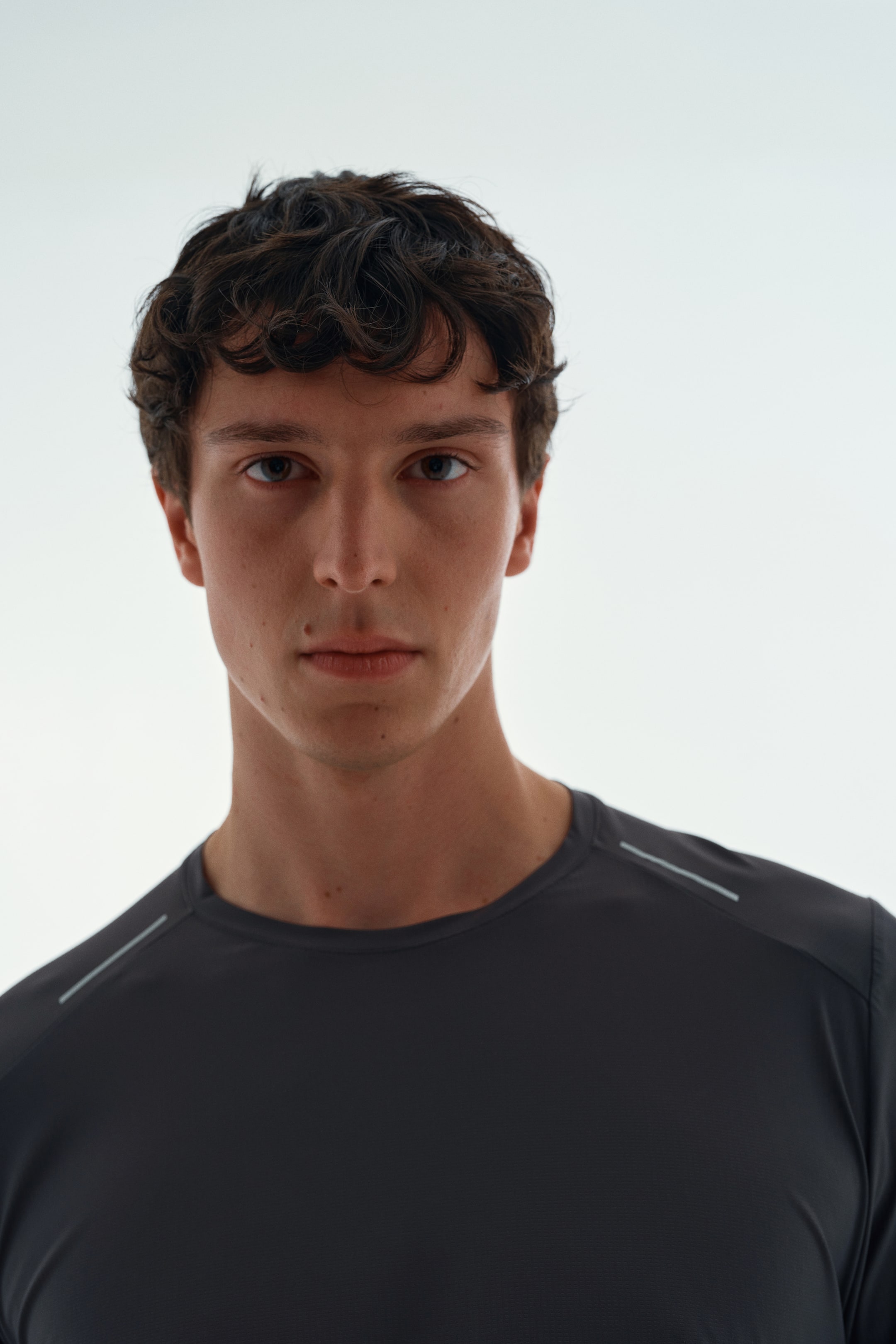 Ver imagen más grande: La modelo lleva puesta una camiseta deportiva gris oscuro de cuello redondo, con finas rayas de color claro a lo largo de las costuras de los hombros.