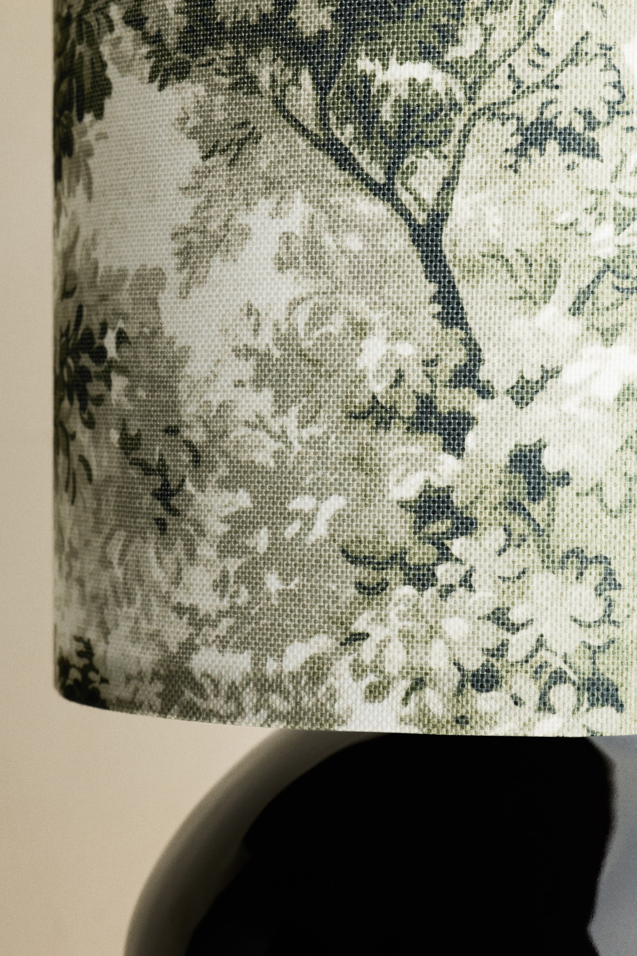 View larger image: A cylindrical fabric lampshade features a detailed tree-and-foliage pattern rendered in shades of olive green, dark green and off-white. The woven texture of the fabric is visible, and the lampshade is viewed from a slight upward angle, showing its lower curve.