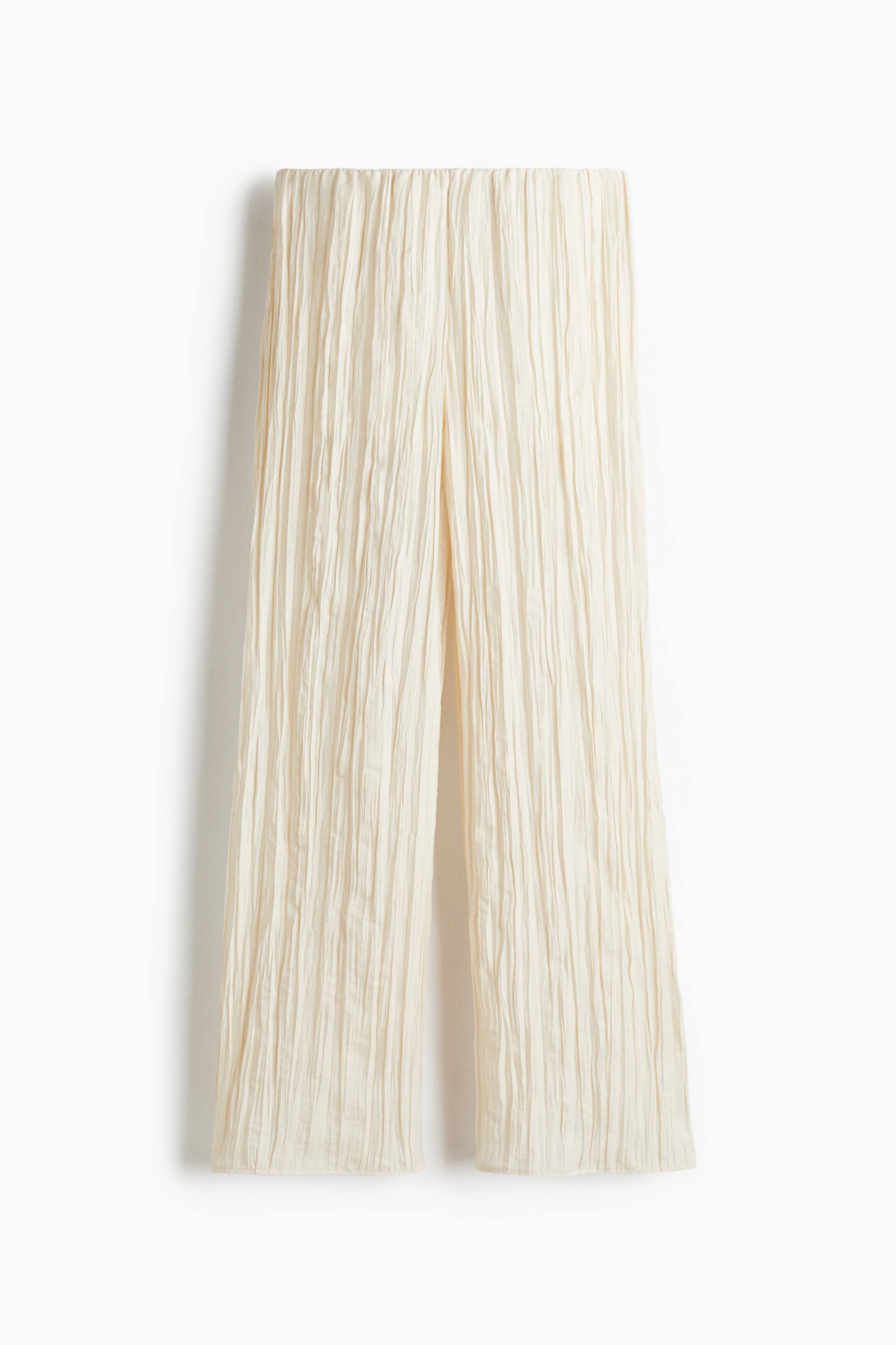 View larger image: The cream-colored pants are featuring a fine vertical plissé texture, an elasticated and gathered waistband, and wide legs, presented from the front.