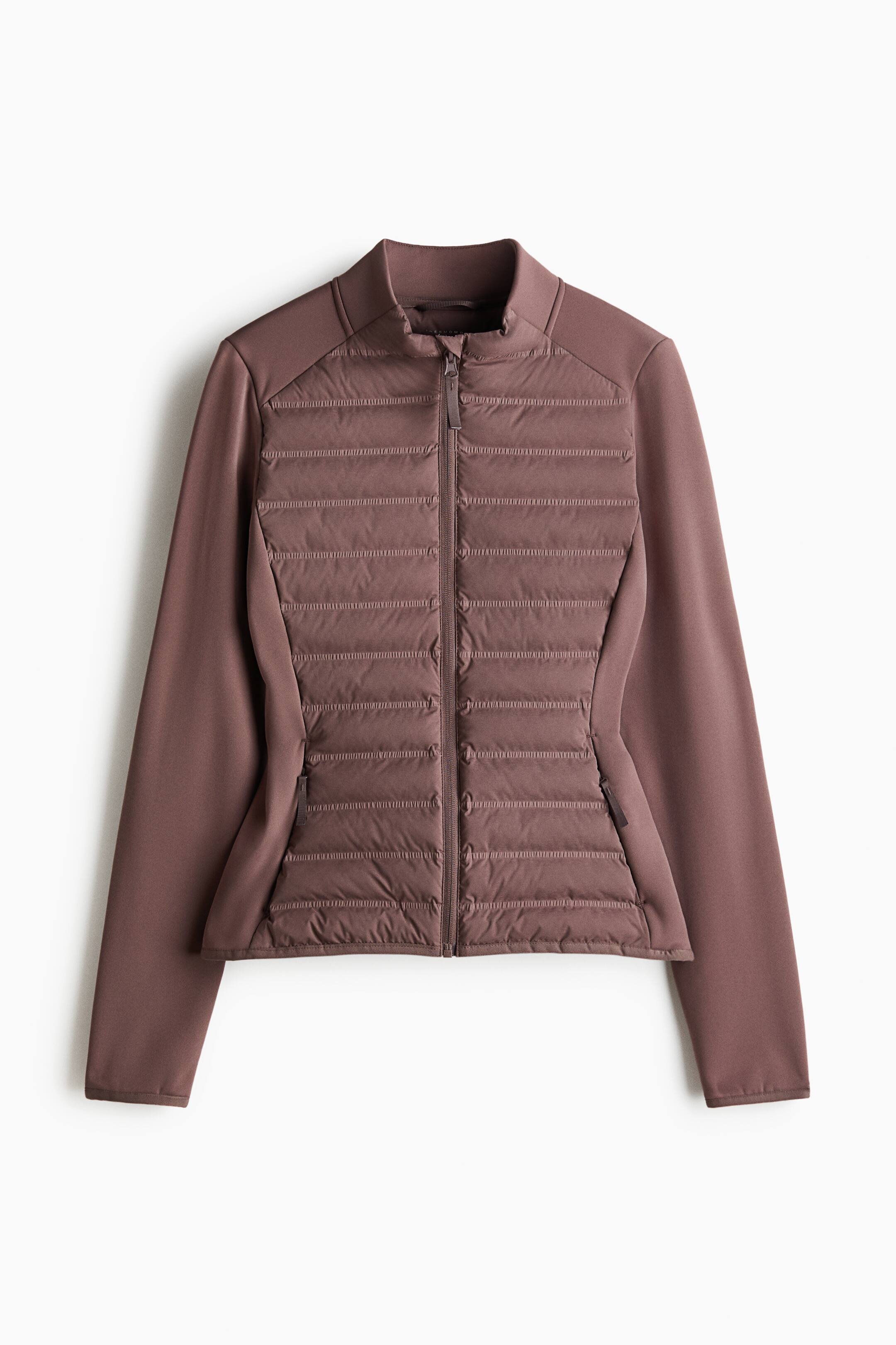 הצגת תמונה גדולה יותר: מעיל היברידי מרופד מוצג מלפנים, בגוון חום-סגלגל. הוא מתאפיין בחזית קדמית מרופדת בקווילט עם תפרים אופקיים בערוצים וצווארון עומד, בעוד שהשרוולים ולוחות הצד עשויים מבד חלק שאינו מרופד. רוכסן מלא יורד לאורך מרכז החזית, ושני כיסים עם רוכסן ממוקמים בחלק התחתון הקדמי.