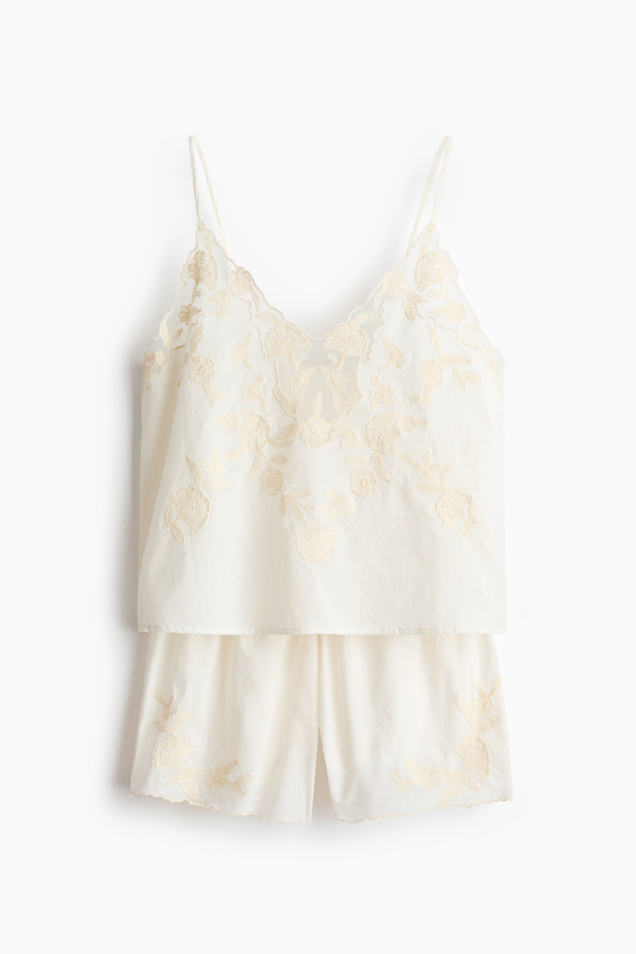 Ver imagen más grande: Un conjunto de pijama crema se presenta de frente, con un camisón de tirantes finos, un escote en V festoneado y un extenso bordado floral en un tono crema ligeramente más oscuro en la parte delantera. Los pantalones cortos a juego muestran bordado floral en el mismo tono cerca del dobladillo festoneado en cada pierna.