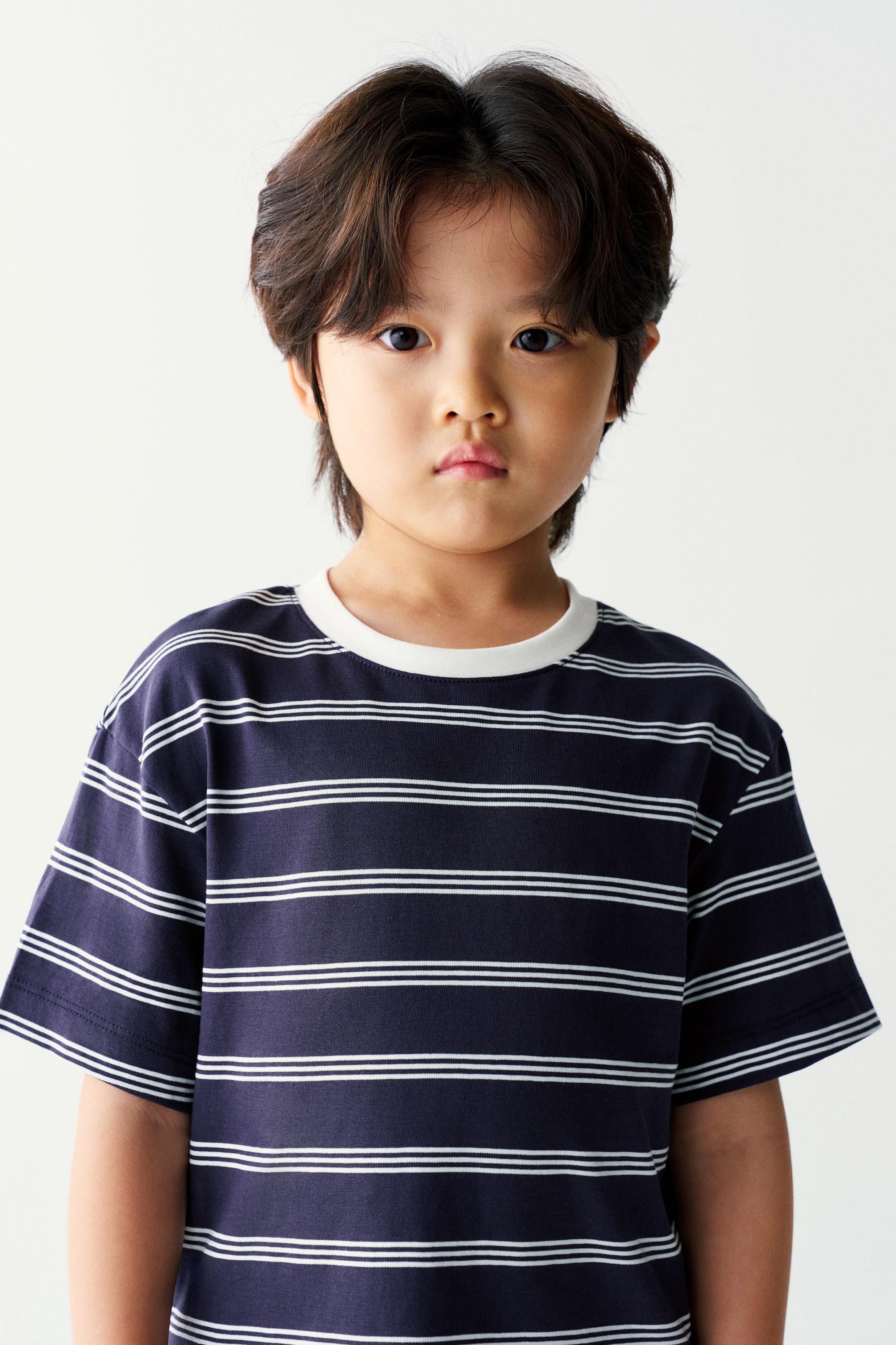 View larger image: The model is wearing a navy blue short-sleeved T-shirt featuring thin double white horizontal stripes and a contrasting white crew neck collar.