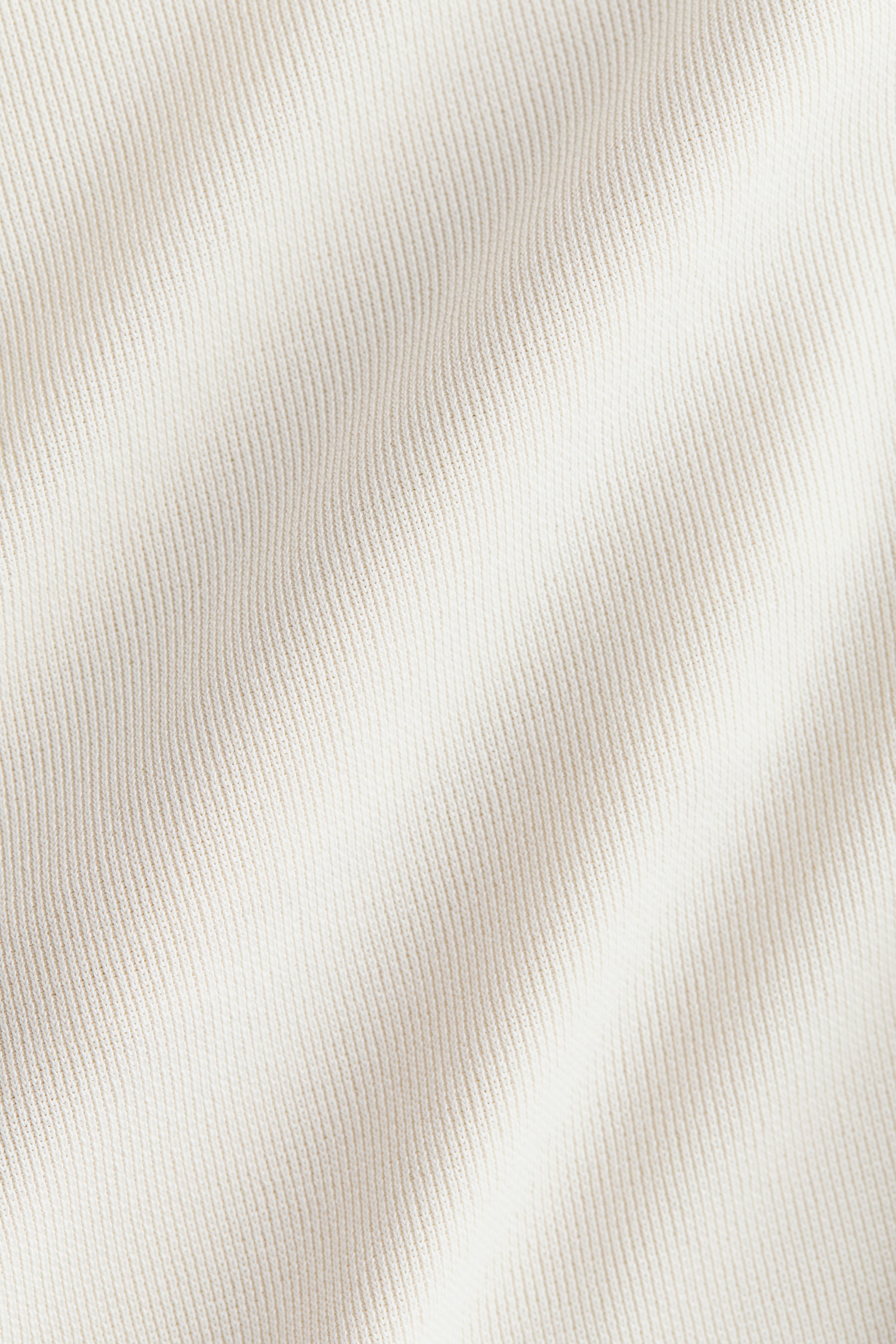 View larger image: The creamy white ribbed knit fabric is displaying vertical ribs and soft folds that create gentle shadows and highlights.