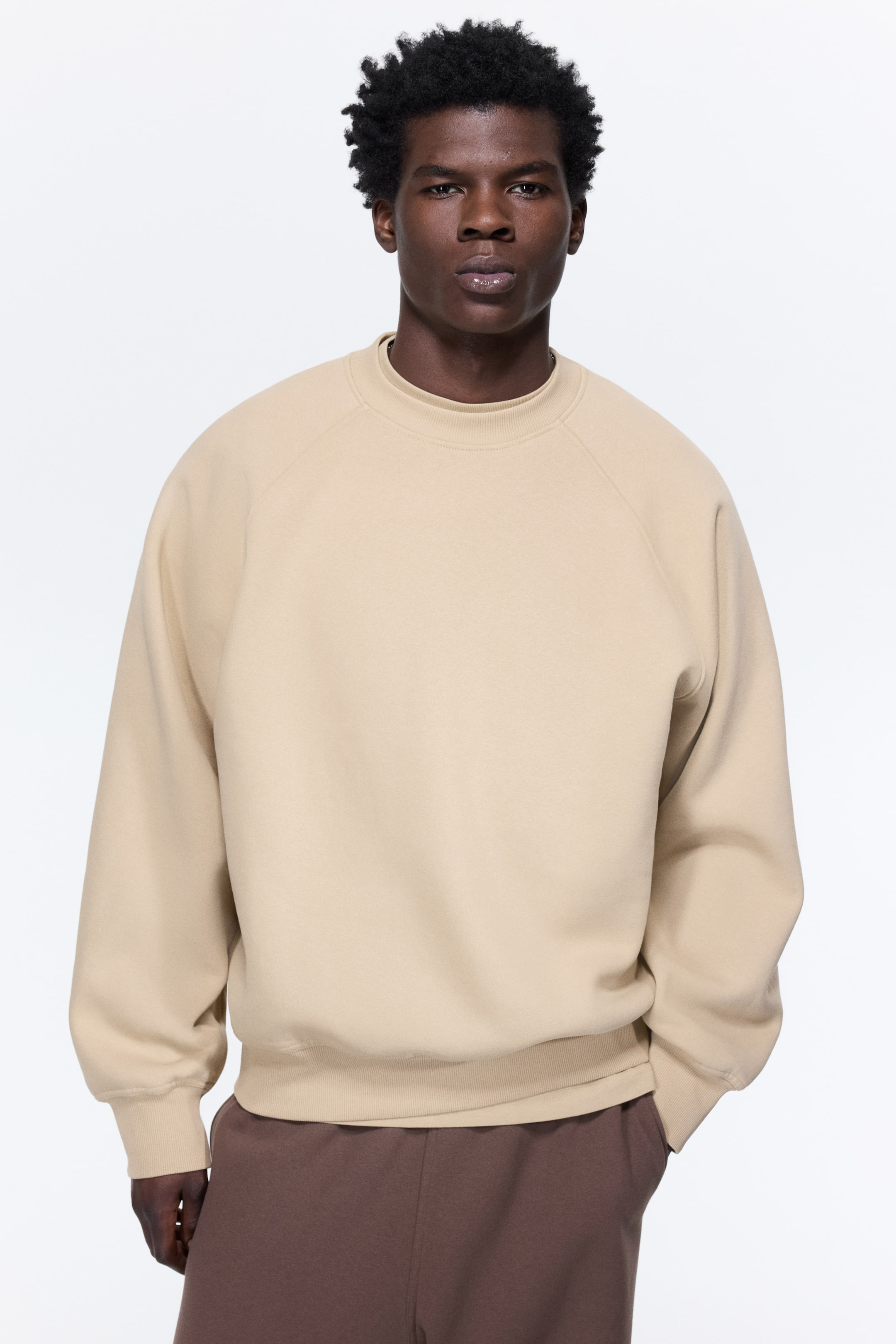 View larger image: An oversized beige top, made from sweatshirt fabric and featuring long raglan sleeves with ribbed trims at the neckline, cuffs, and hem, is being worn by the model. The model is wearing the top with brown pants.