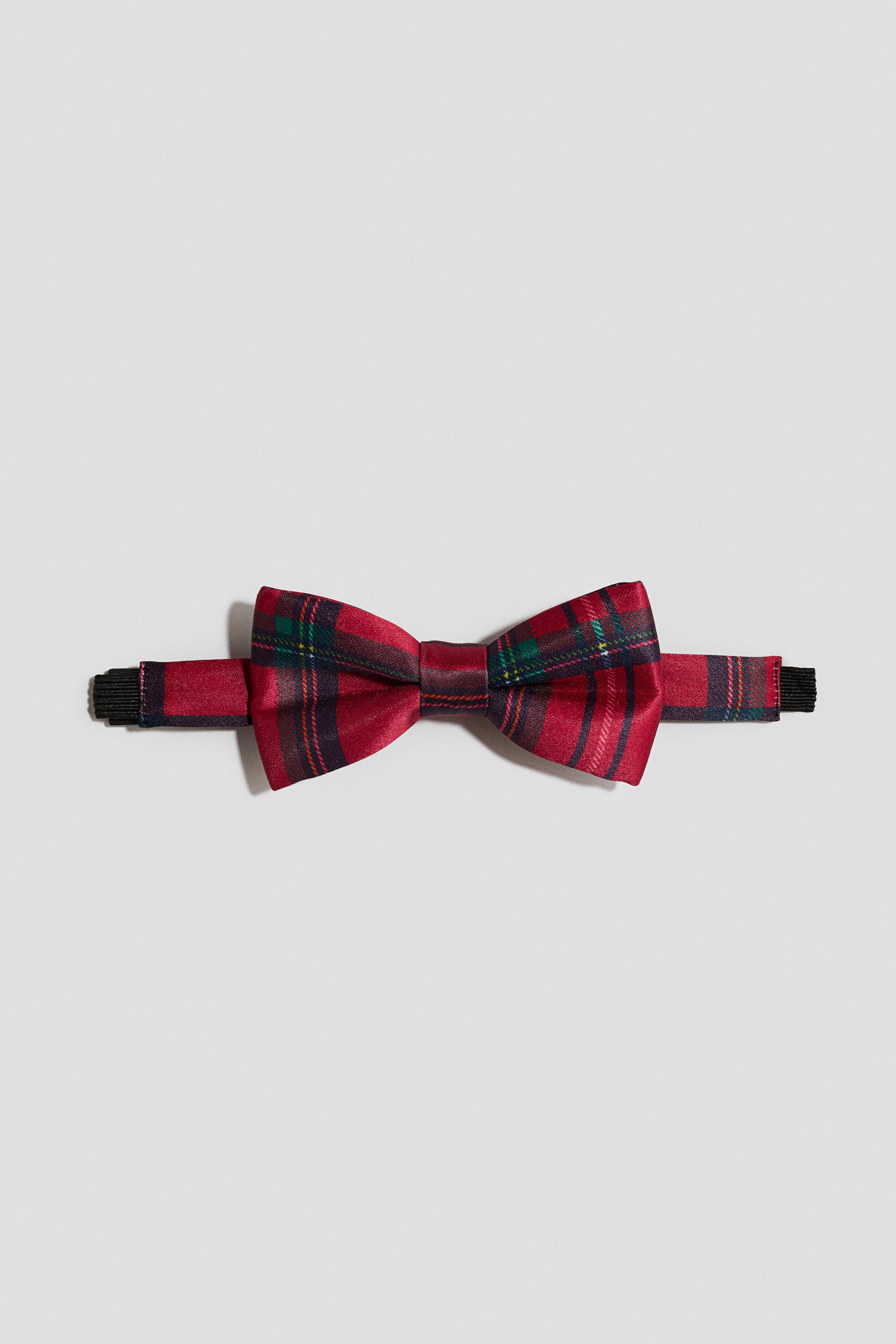 Agrandir l'image: Un nœud papillon pré-noué à motif tartan rouge est présenté de face, mettant en valeur son tissu satiné lisse et sa forme de nœud structurée. Le nœud papillon est posé à plat, dévoilant une bride de cou assortie recouverte du même tissu, avec des extrémités élastiques noires de chaque côté.