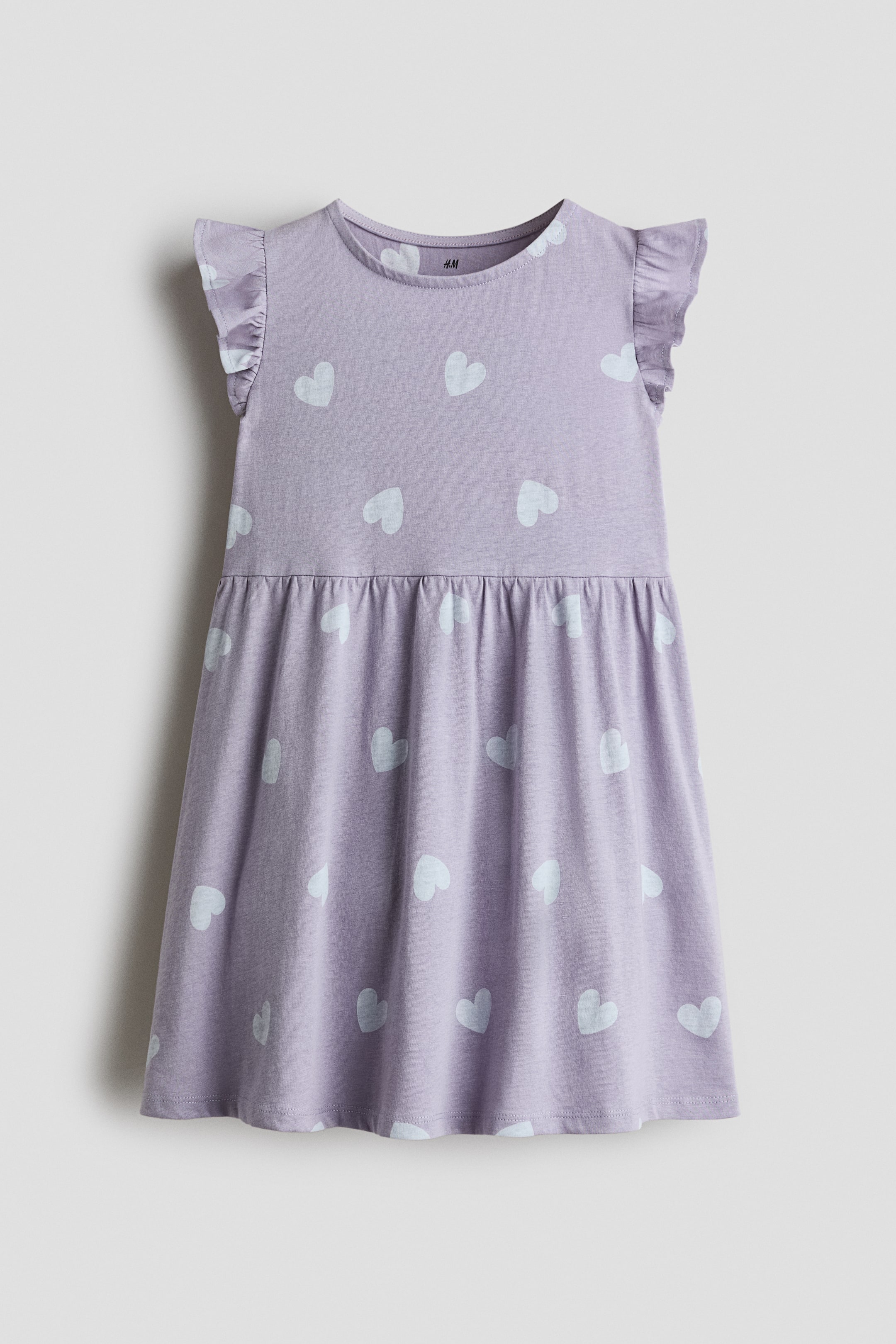 View larger image: A light purple cotton jersey dress is shown from the front, featuring an all-over white heart pattern, a crew neckline, flutter sleeves, and a gathered seam at the waist.