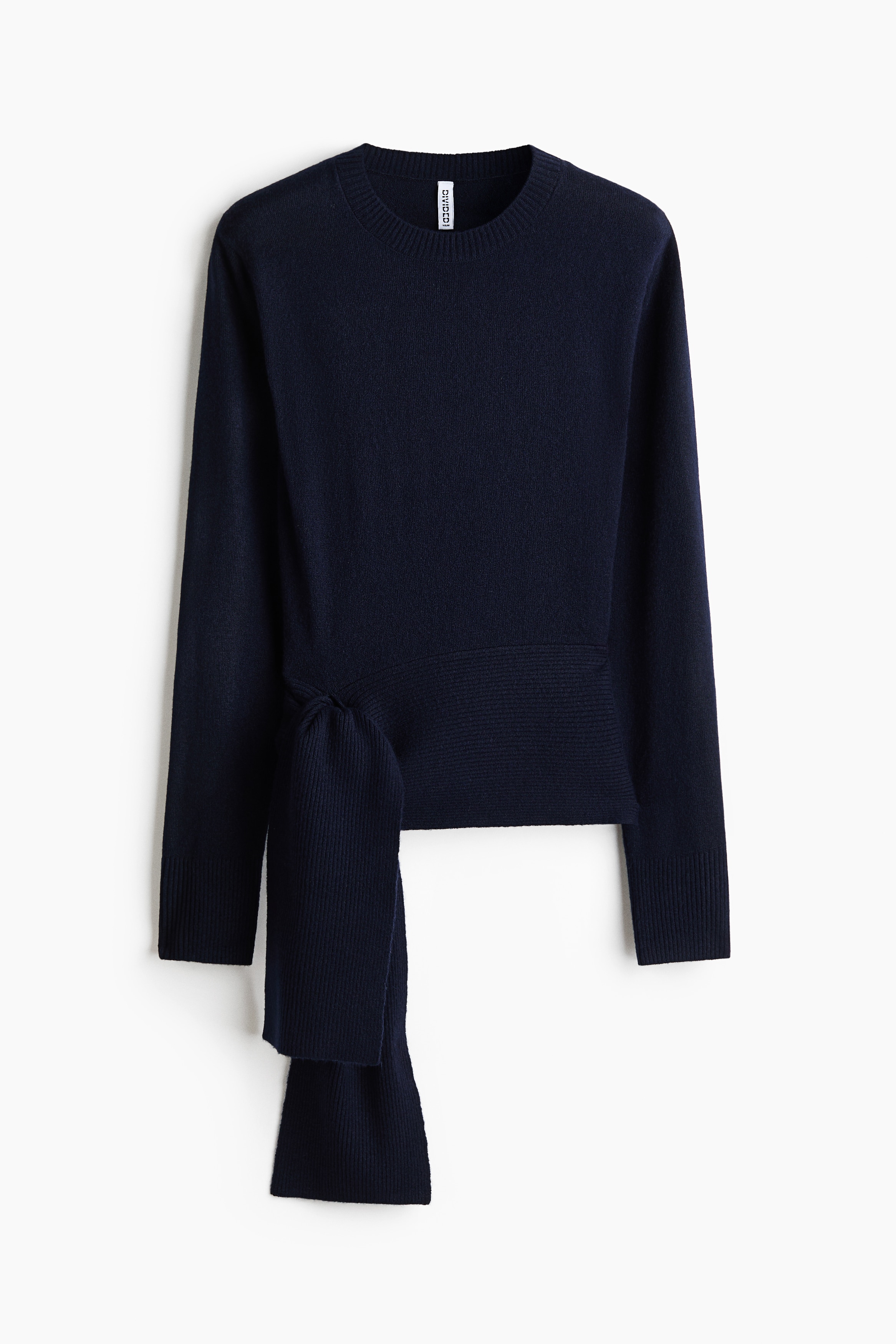 A dark navy blue knit sweater with a ribbed crew neckline and a wide tie detail at the front hem is being worn by the model. The sweater is paired with a blue plaid skirt.