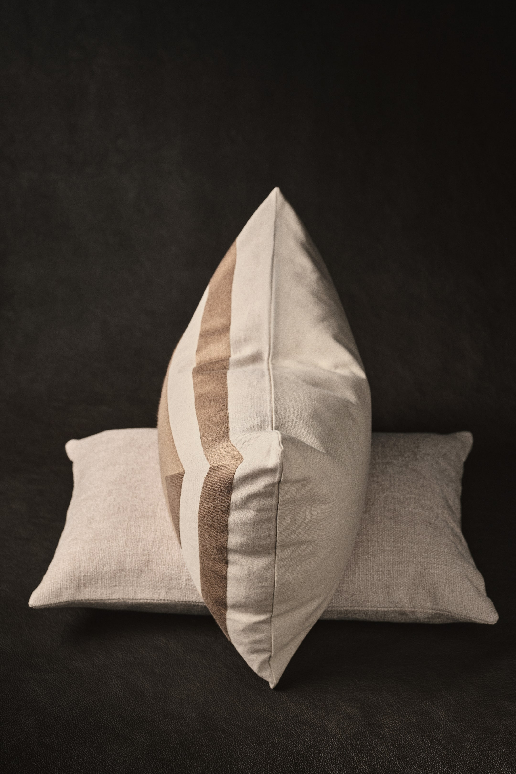View larger image: A light beige pillow with vertical brown stripes is positioned on its side, slanting towards the right. It is placed on another pillow with a lighter textured beige, which is lying flat.