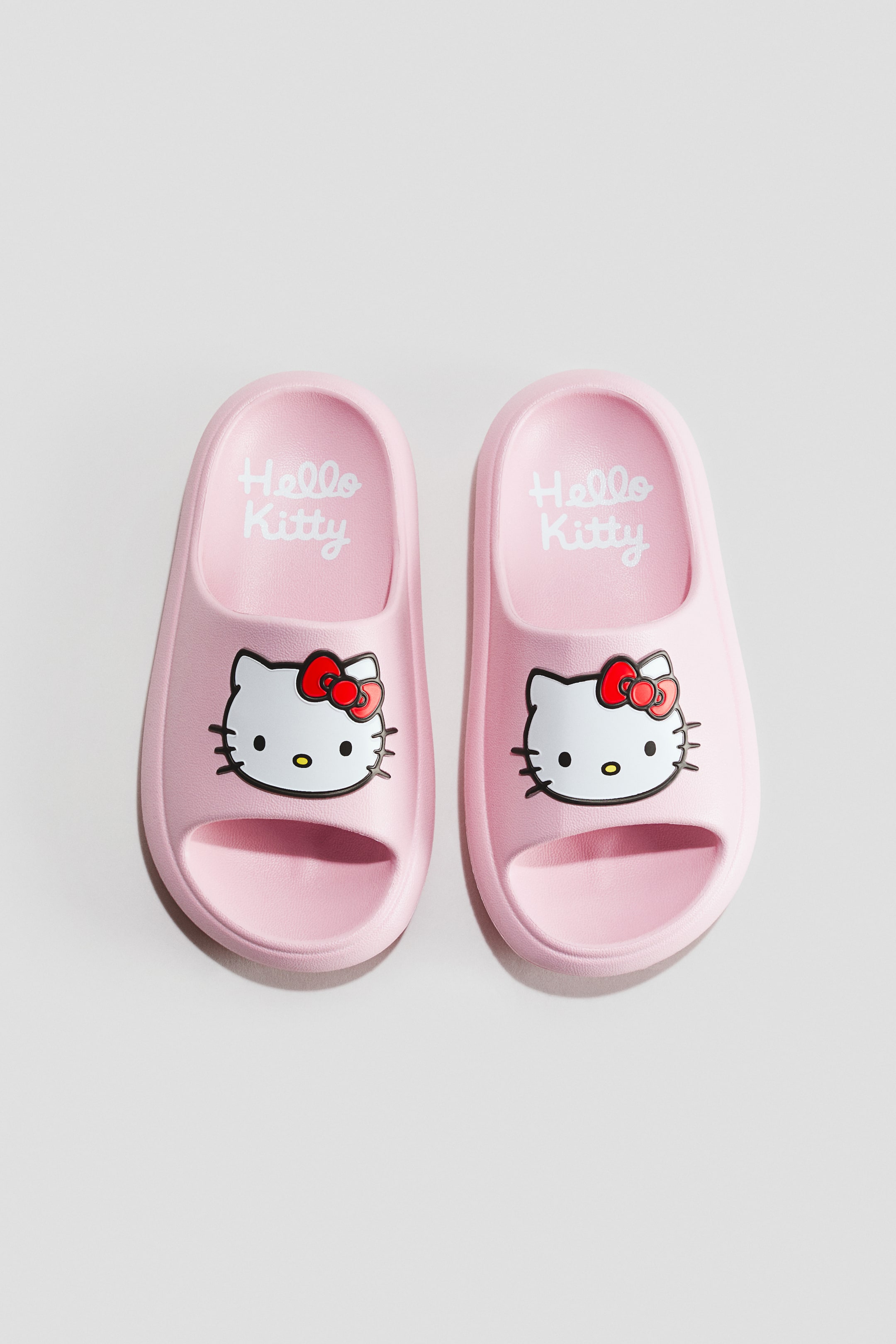 Visualizza l'immagine ingrandita: Un paio di ciabatte da piscina rosa modellate è mostrato frontalmente. Ogni ciabatta presenta un volto del personaggio Hello Kitty bianco sulla fascia superiore, e le parole "Hello Kitty" sono visibili sulla soletta rosa.