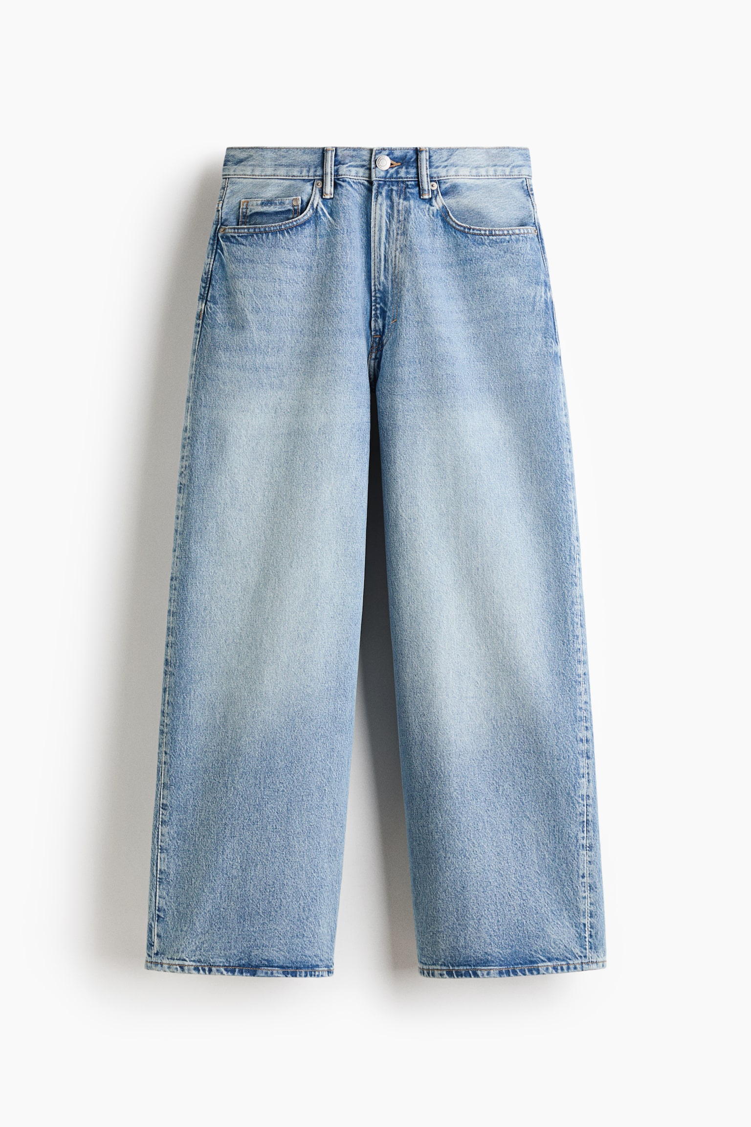 A pair of light blue rigid cotton denim jeans is being presented from the front, displaying a regular waist, a zip fly, and front pockets. The jeans are exhibiting a baggy fit with rounded legs, a dropped crotch, and a long, wide hem designed to stack at the ankle. - 1