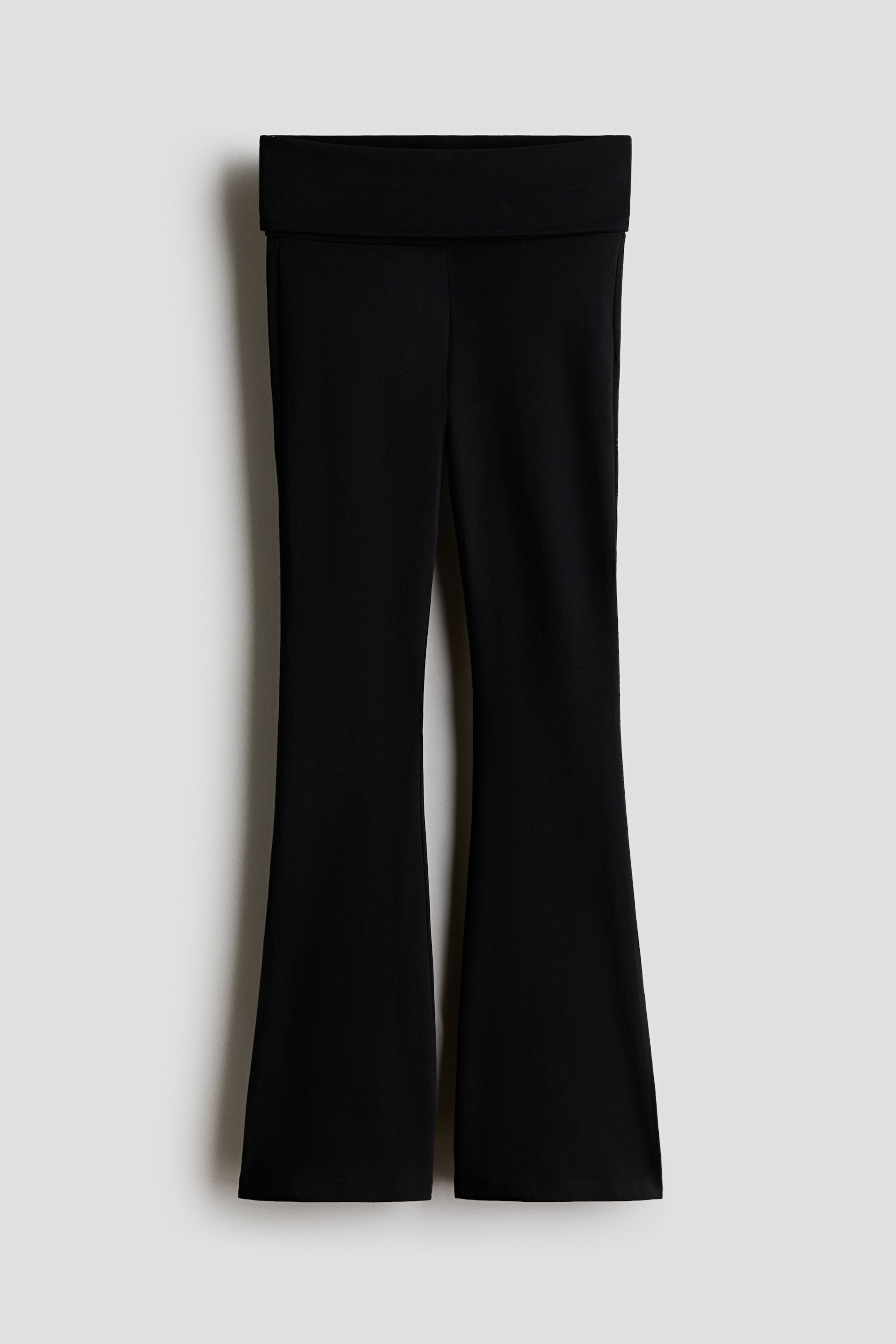View larger image: Black flared pants feature a wide, folded waistband and flare out from the knee to the hem.