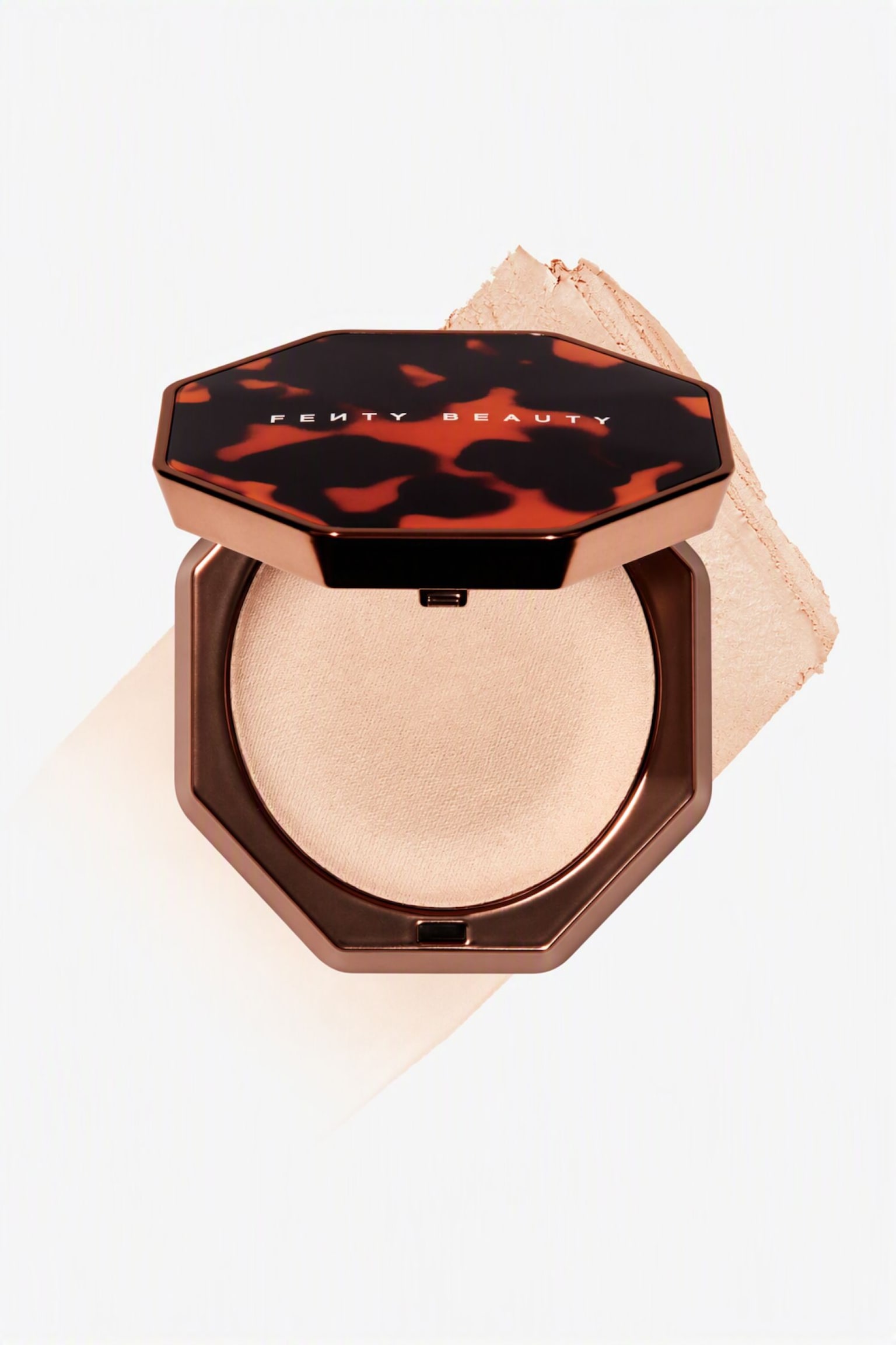 En Ã¥ben, ottekantet bronzekompakt med et lyst beige presset pudder hviler pÃ¥ en diagonal, struktureret prÃ¸ve af den samme cremefarvede makeup. Det hÃ¦vede lÃ¥g har et skildpaddemÃ¸nster i mÃ¸rkebrune og ravfarvede nuancer med "FENTY BEAUTY"-logoet trykt i hvidt. - 1