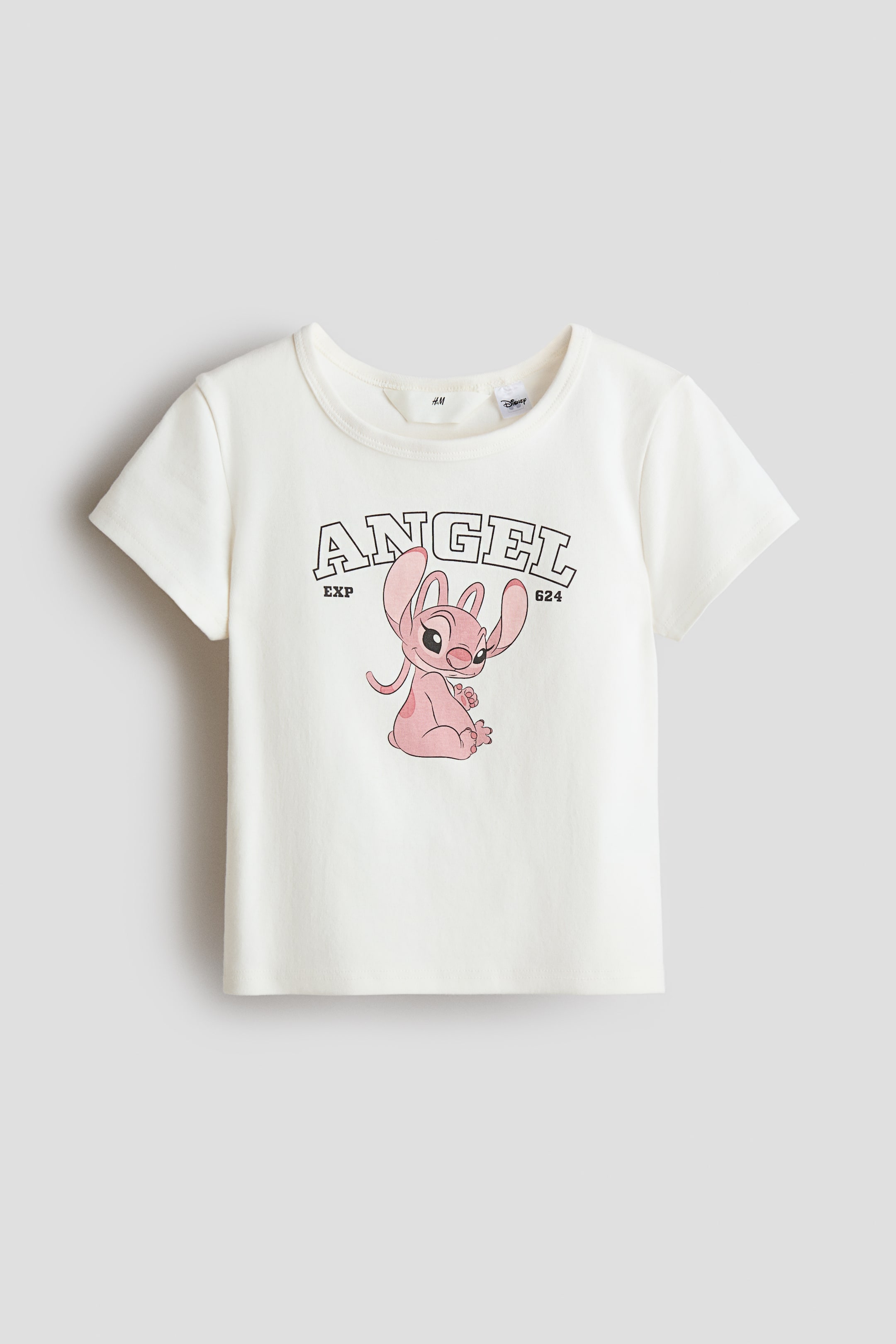 View larger image: An off-white short-sleeved t-shirt is presenting its front, featuring a ribbed crew neck. A graphic print is dominating the front, depicting the word "ANGEL" in a collegiate-style font with "EXP" and "624" below it, and a pink cartoon character, Angel, is sitting beneath the text.