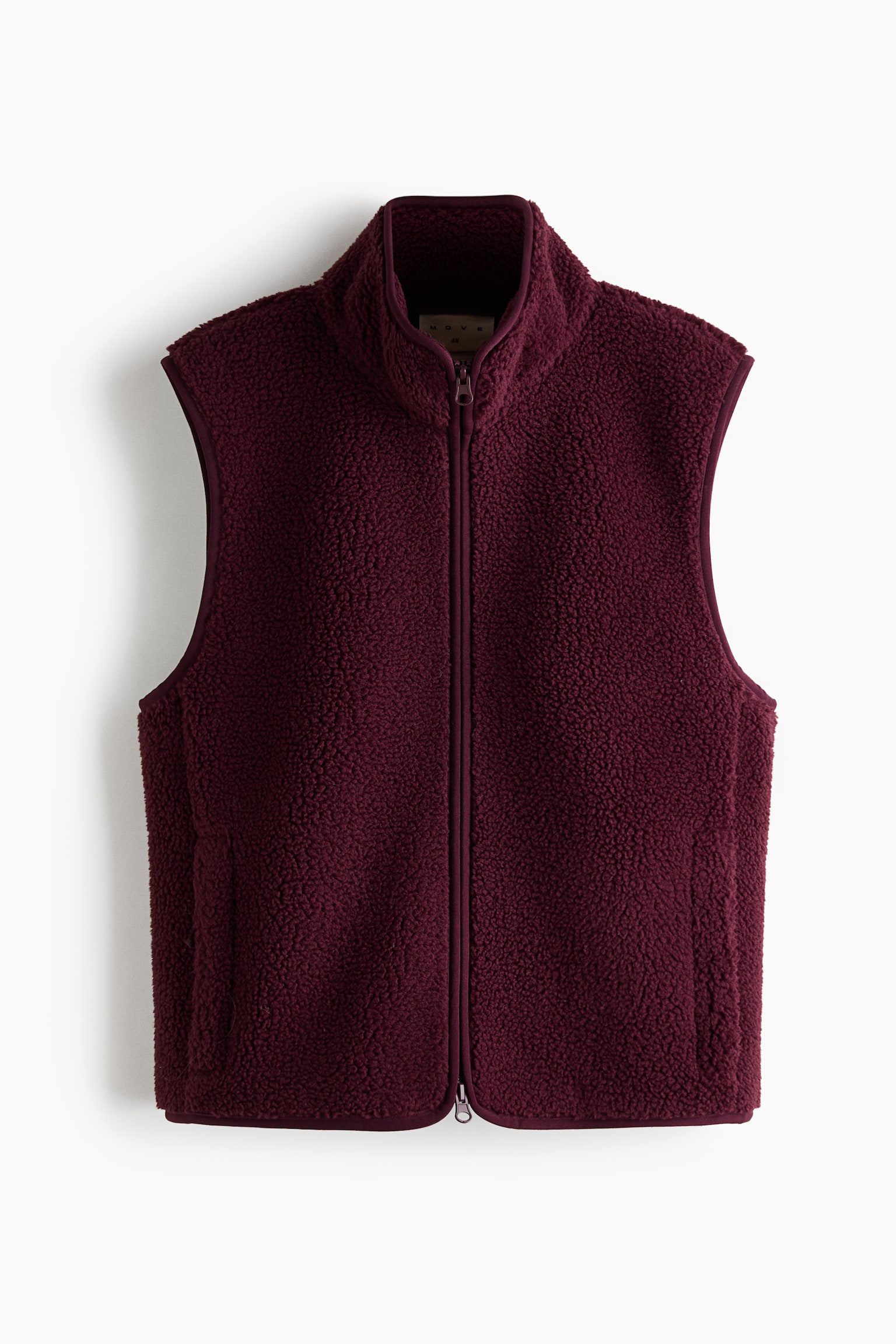 A burgundy teddy fleece activewear vest is shown from the front, featuring a high collar, a full-length front zipper, and a textured, curly pile finish. The vest has elasticated binding along the armholes, collar, and straight hem, with vertical welt pockets integrated at the sides.