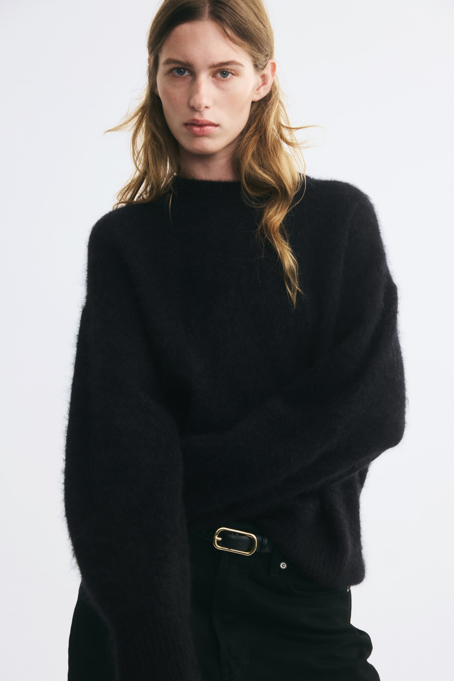 A black oversized jumper knitted in a fuzzy wool is shown from the front, featuring a round, rib-trimmed neckline and dropped shoulders. The long sleeves end in ribbed cuffs, and the hem has a matching ribbed finish. - 1