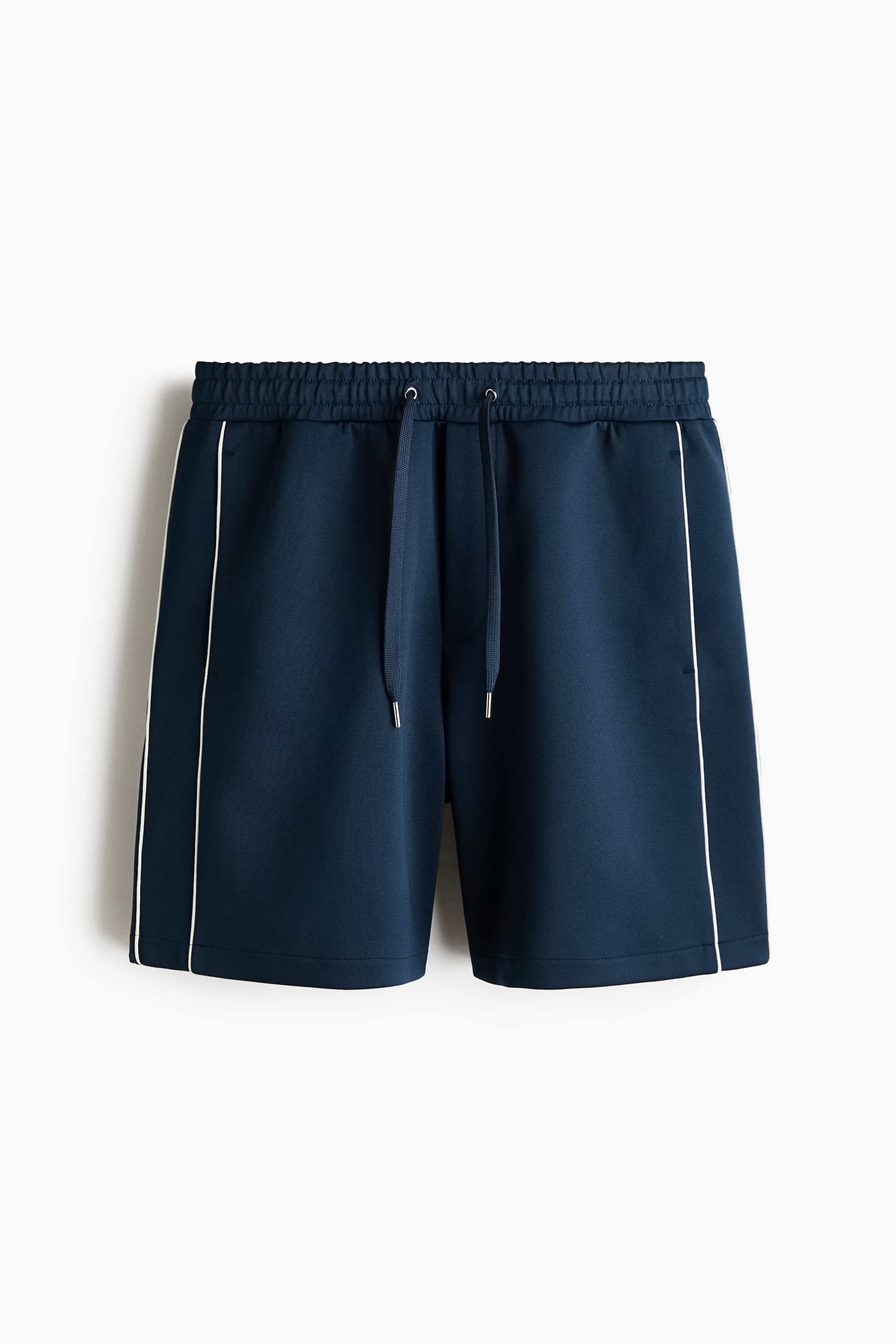 View larger image: Navy blue shorts feature an elastic waistband with a visible navy drawstring and silver-toned tips, while white piping runs vertically down the outer side seams of both legs.