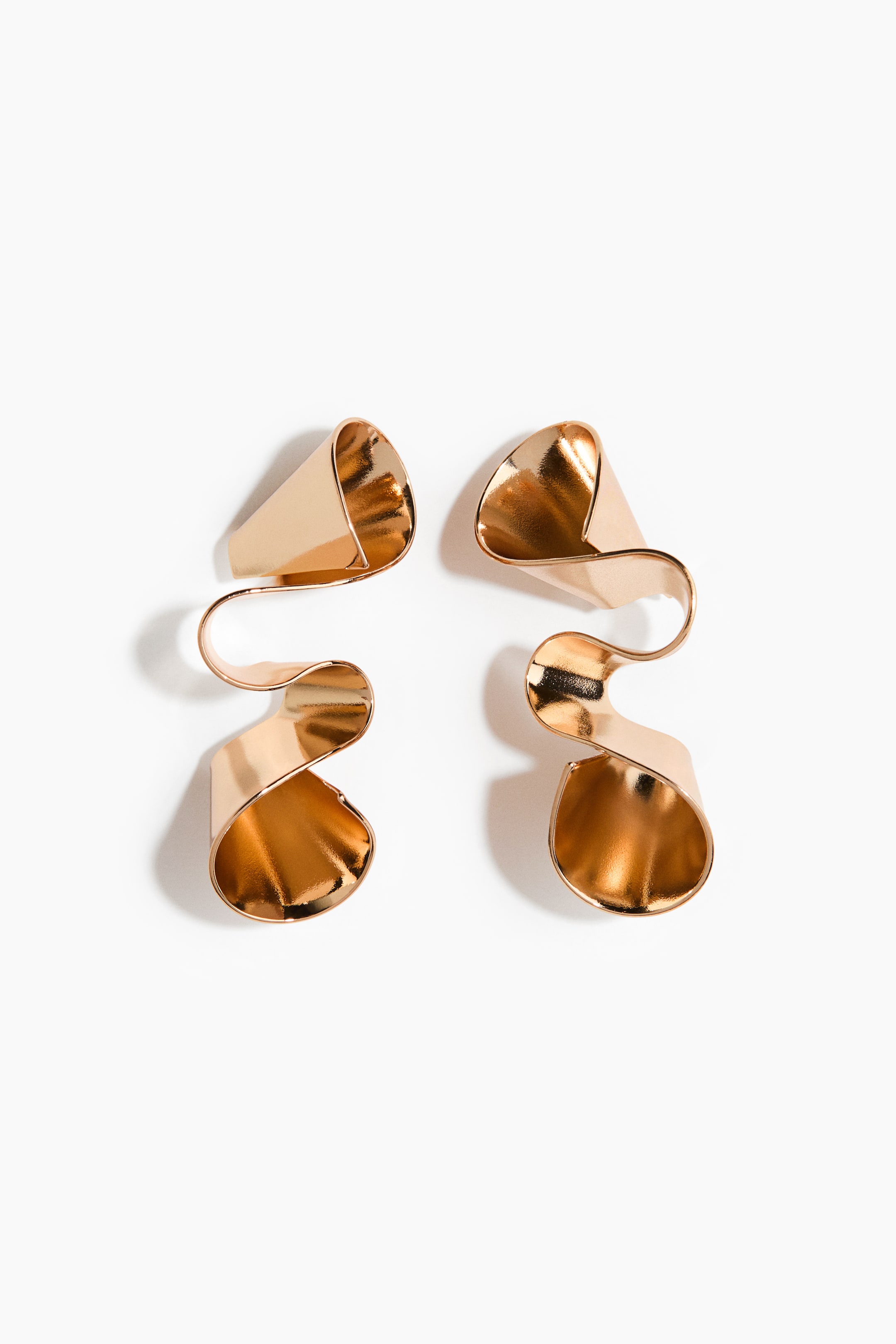 View larger image: A pair of gold-toned earrings lies flat, showcasing a wavy, sculptural design. Each earring features two wider, cup-like sections connected by a narrower S-shaped curve.