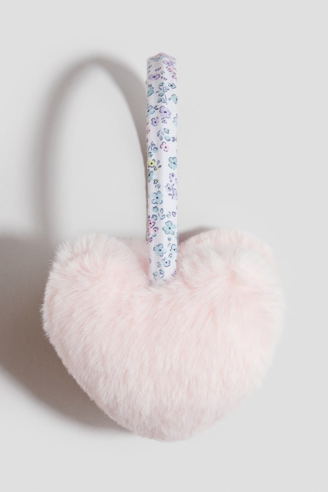 Padded earmuffs are featuring a heart-shaped cup made of soft, fluffy pink fabric. A narrow headband, covered in a white fabric with a small multi-colored floral pattern, is connecting to the top of the cup. - 1