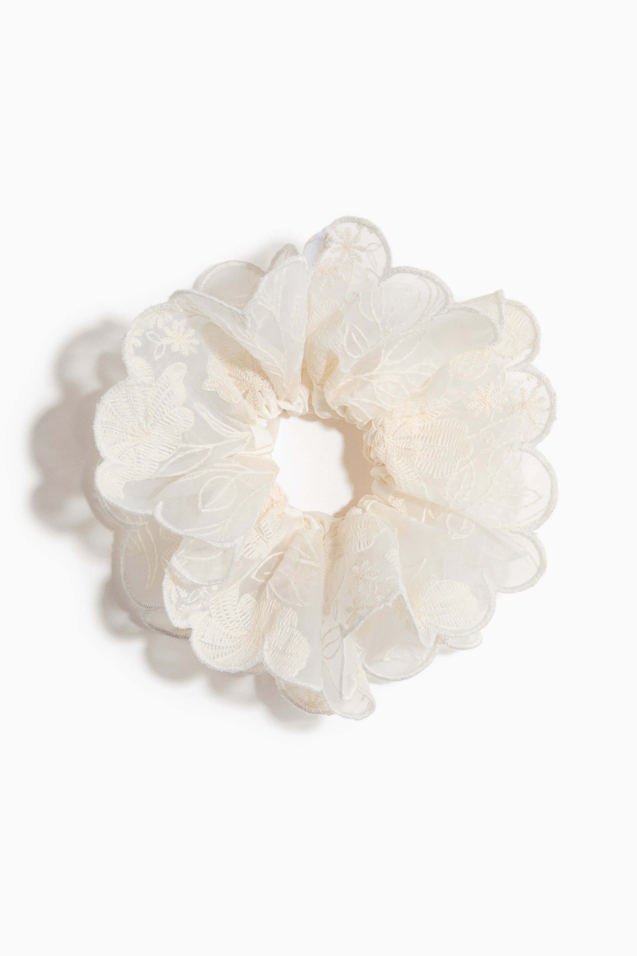 Grotere afbeelding bekijken: Een off-white scrunchie is zichtbaar van voren, met meerdere gerimpelde lagen stof. Het toont doorschijnende buitenlagen met verfijnde bloemenborduursels en geschulpte randen.